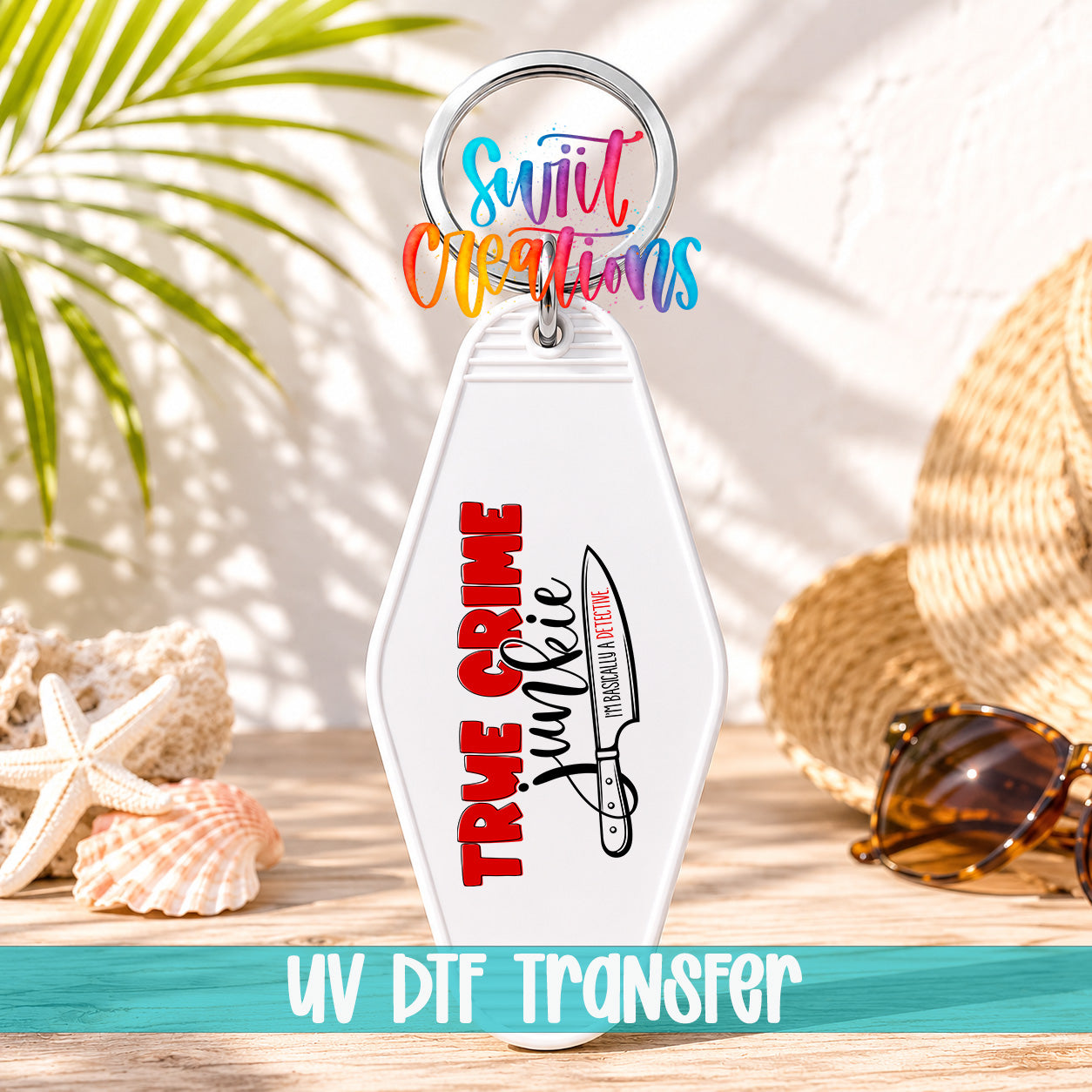 A white keychain with a colorful design and text, placed on a wooden surface with sunglasses and a straw hat in the background.