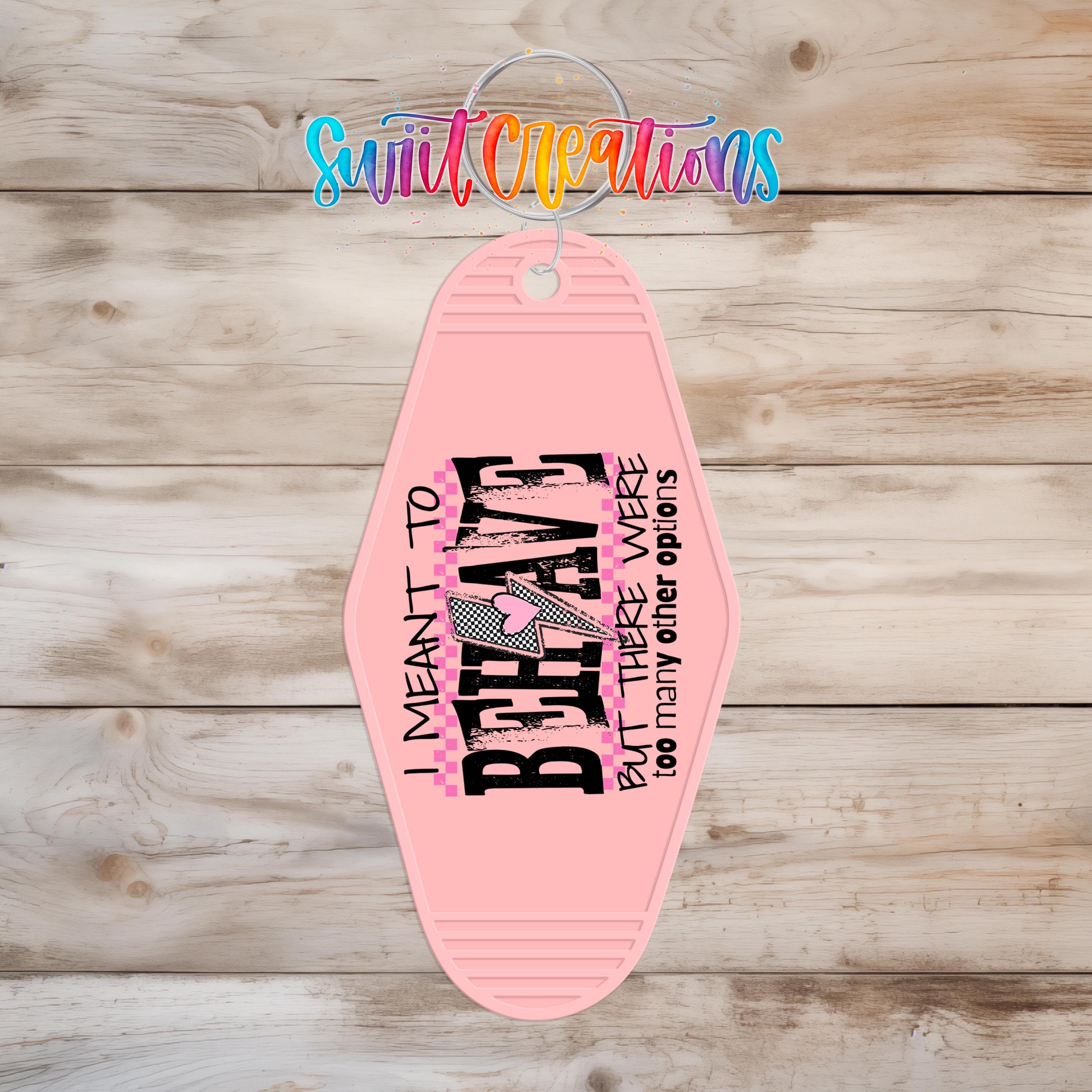 A pink keychain with a text design on it, hanging on a wooden surface.