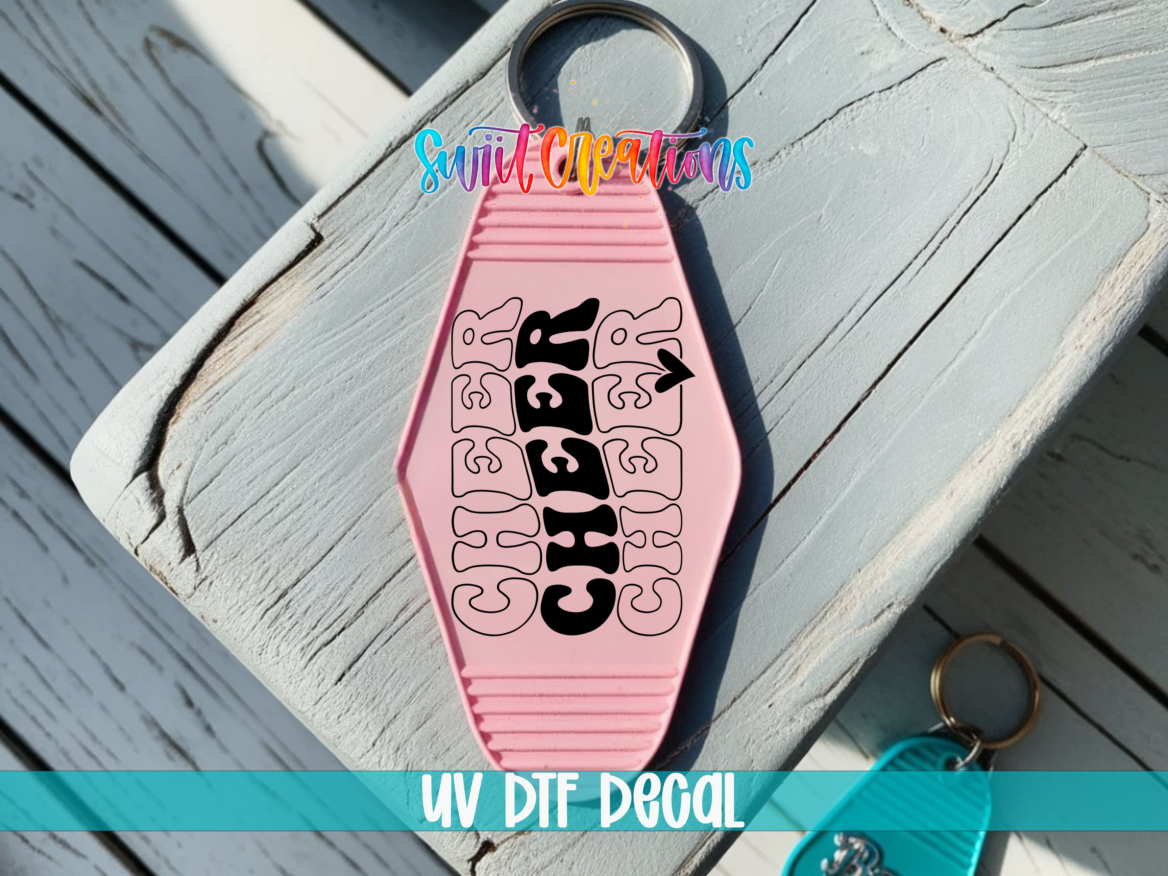 A pink keychain with the word "CHEER" printed on it, placed on a wooden surface.