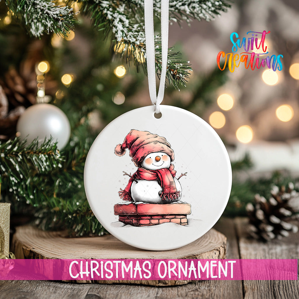 A white Christmas ornament featuring a snowman is hanging from a tree branch, with a blurred background of lights and greenery.