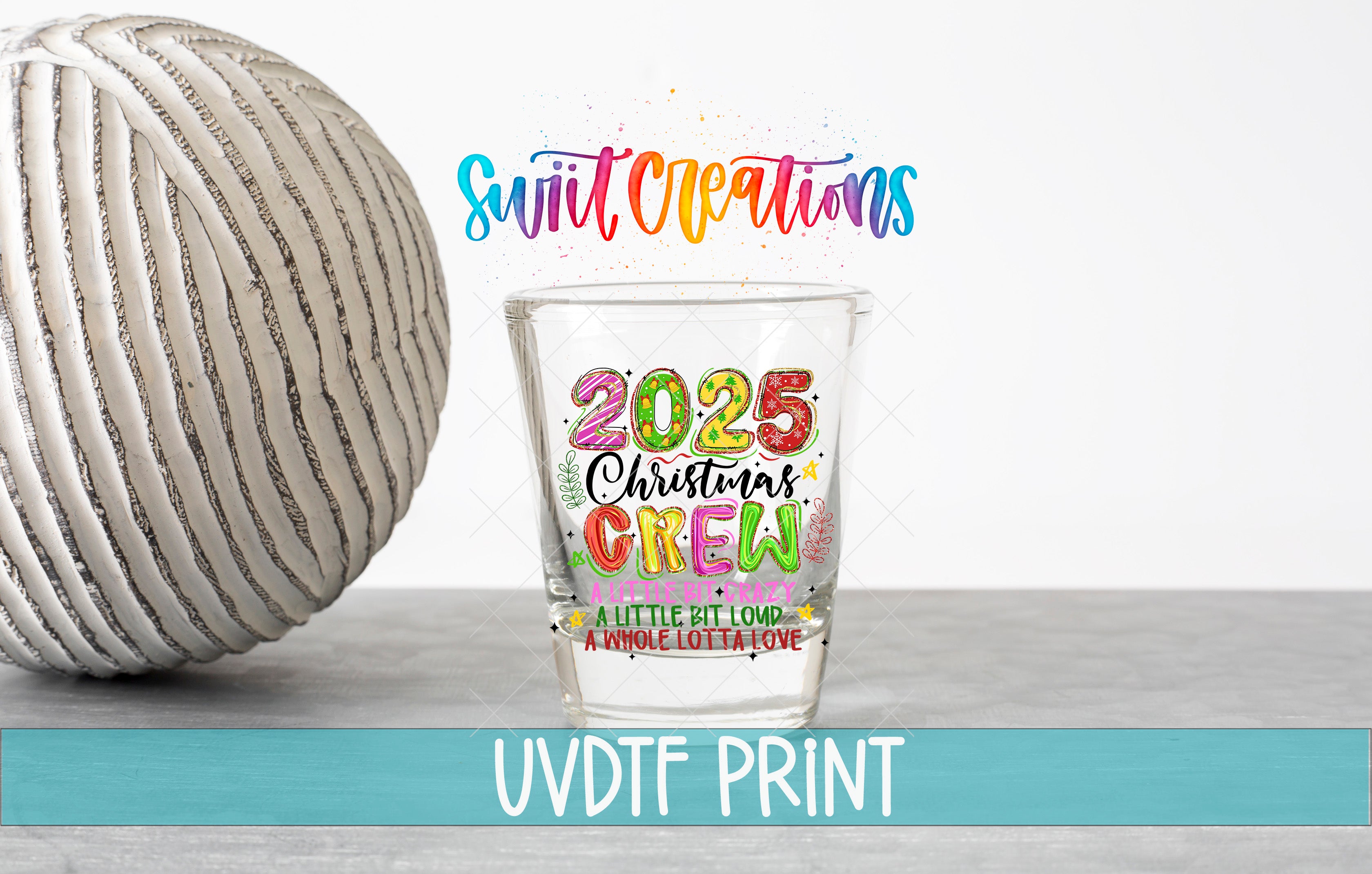 a shot glass with a colorful design and text, placed on a table next to a white ball.