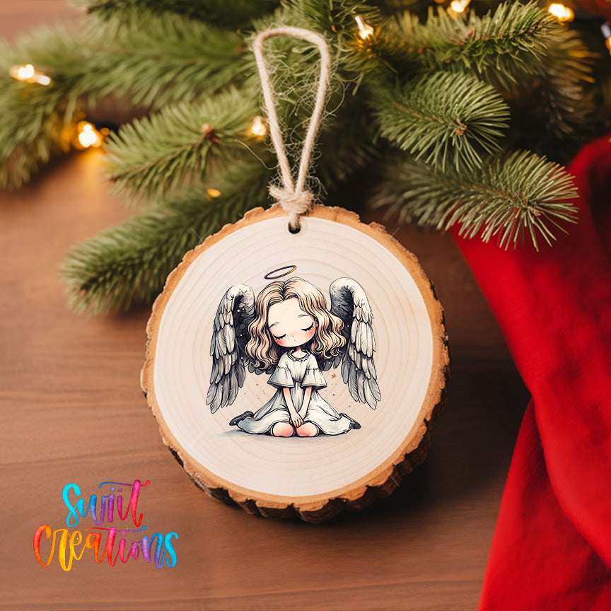 A wooden ornament with a picture of a smiling angel with wings is hanging on a Christmas tree.