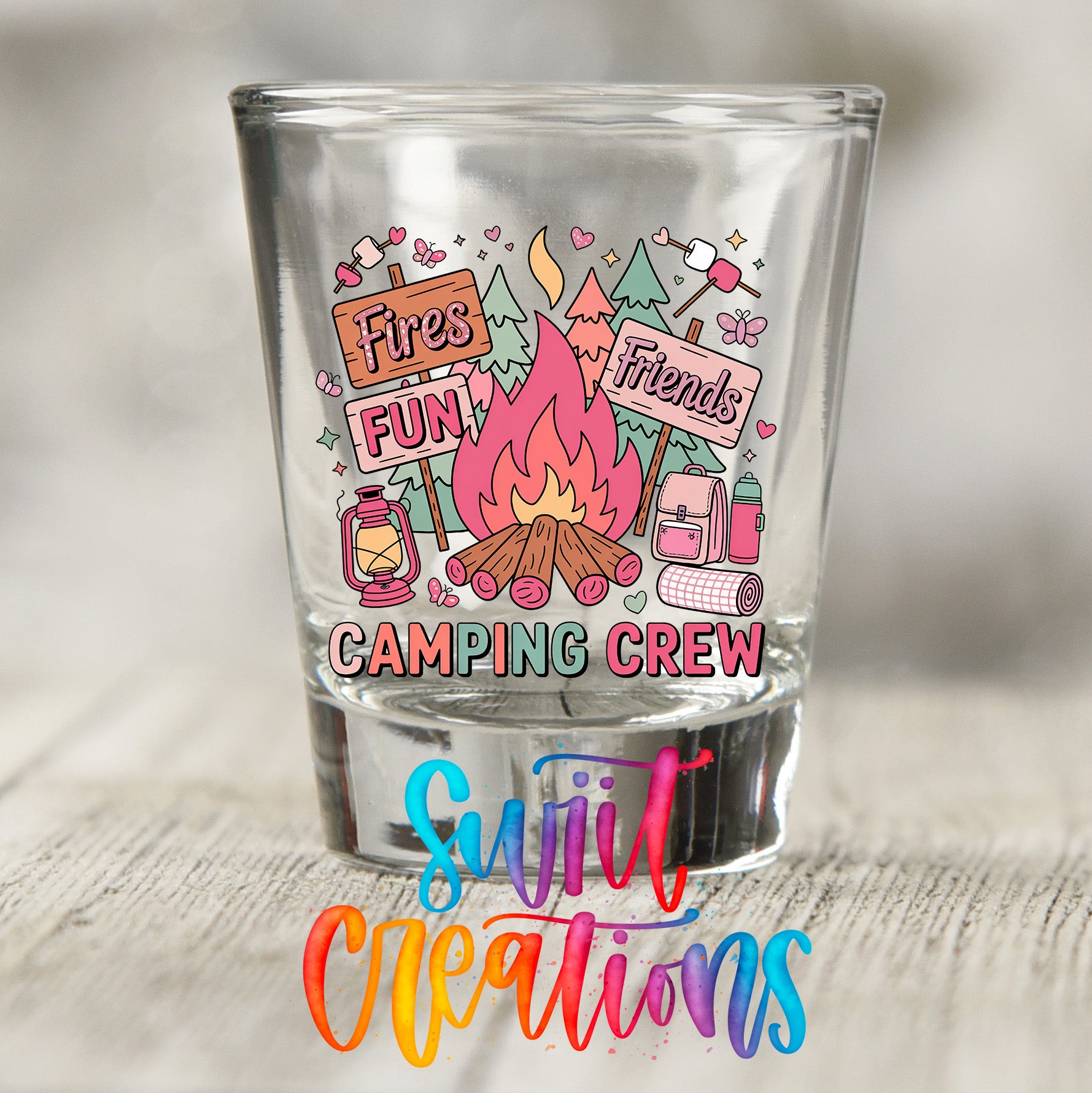 A shot glass with a colorful illustration of camping-related items and text, including a campfire, camping equipment, and the phrase "Fires Fun Friends Camping Crew".