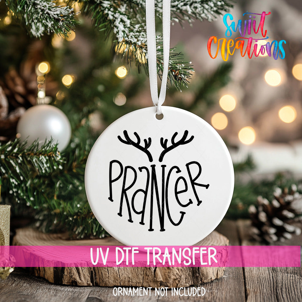 A white ornament with the word "PRANCE" written on it, hanging on a Christmas tree.