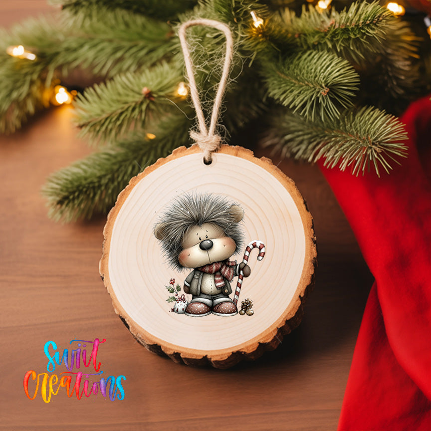 A wooden ornament featuring a cartoon hedgehog holding a candy cane and surrounded by pine branches, with a red ribbon and a "Swift Creations" logo in the background.