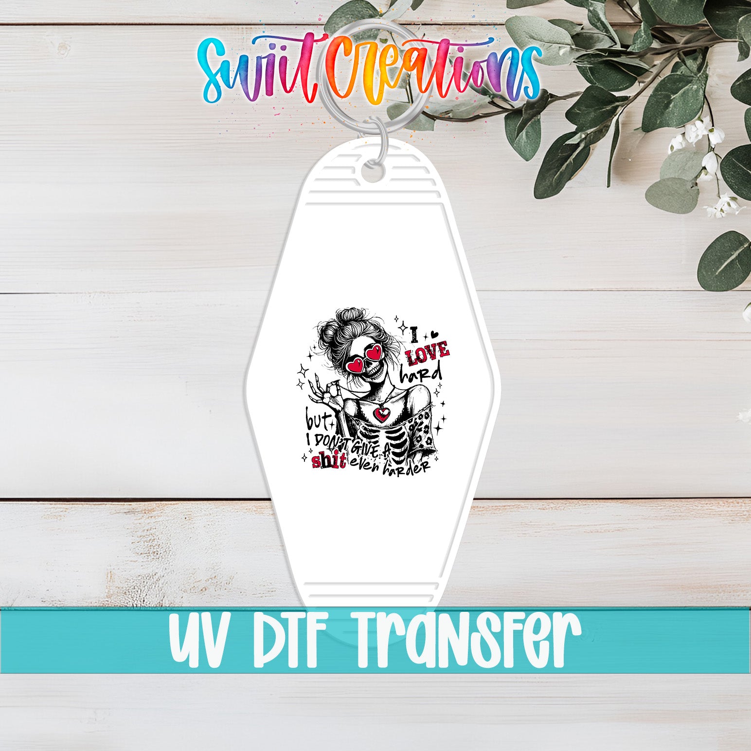 A keychain with a skull design and text, placed on a wooden surface with greenery in the background.