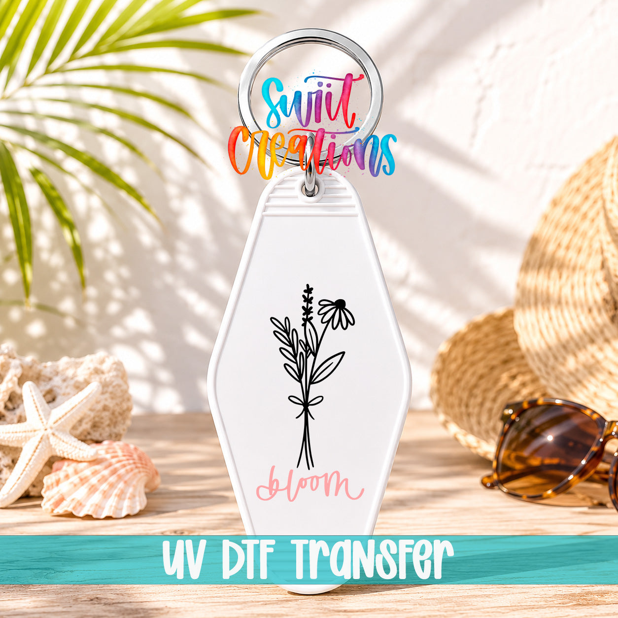 A keychain with a floral design and the text "Blom" printed on it, placed on a wooden surface with sunglasses and a straw hat in the background.