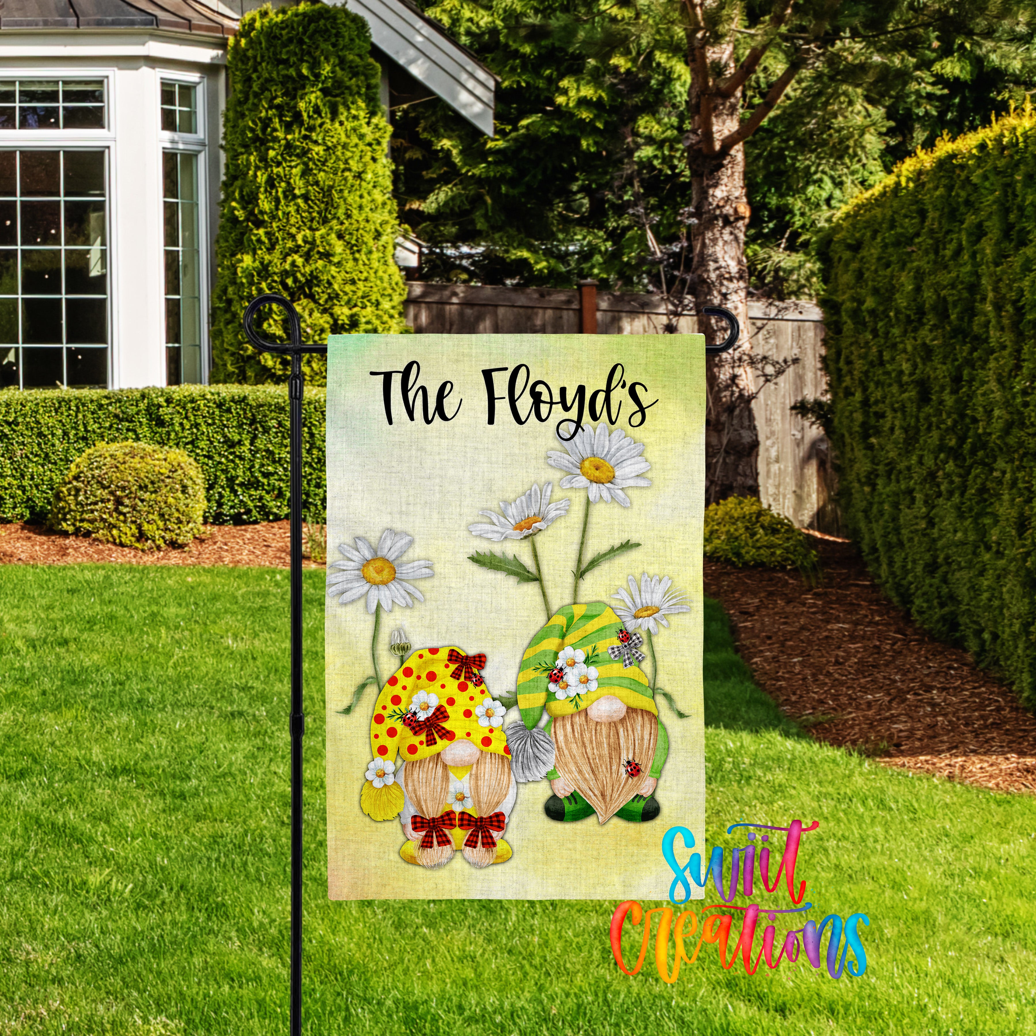 A garden sign featuring two gnomes with flowers, placed in a grassy yard with a house and trees in the background.