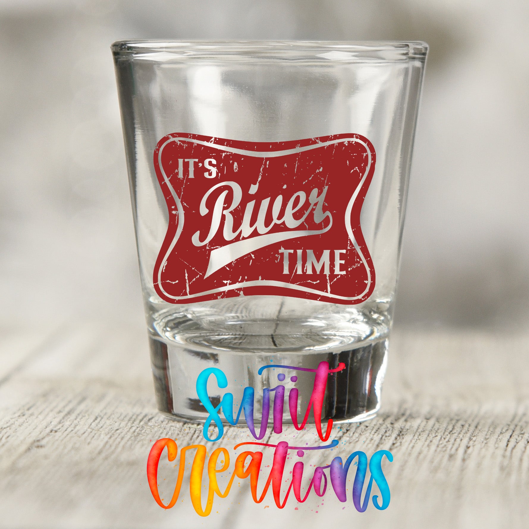 A shot glass with a red and white label that says "It's River Time" and "Sujiv Creations" written below it.