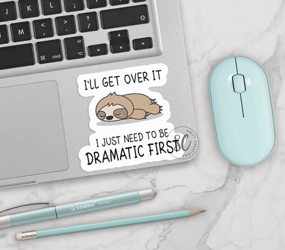 Dramatic Sloth vinyl sticker on a silver laptop next to a mint mouse and pens