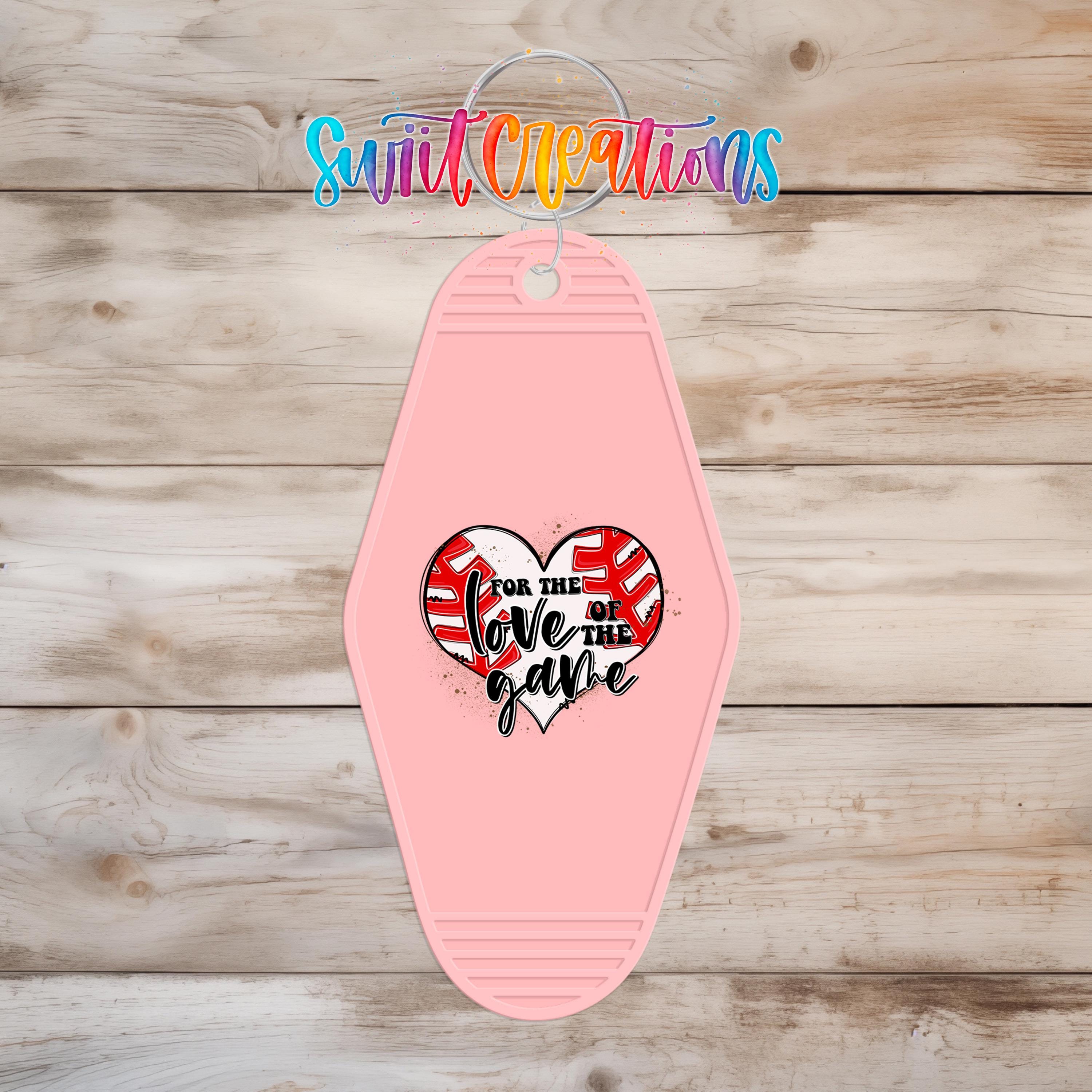 A pink keychain with a heart-shaped design and text on it, hanging on a wooden surface.