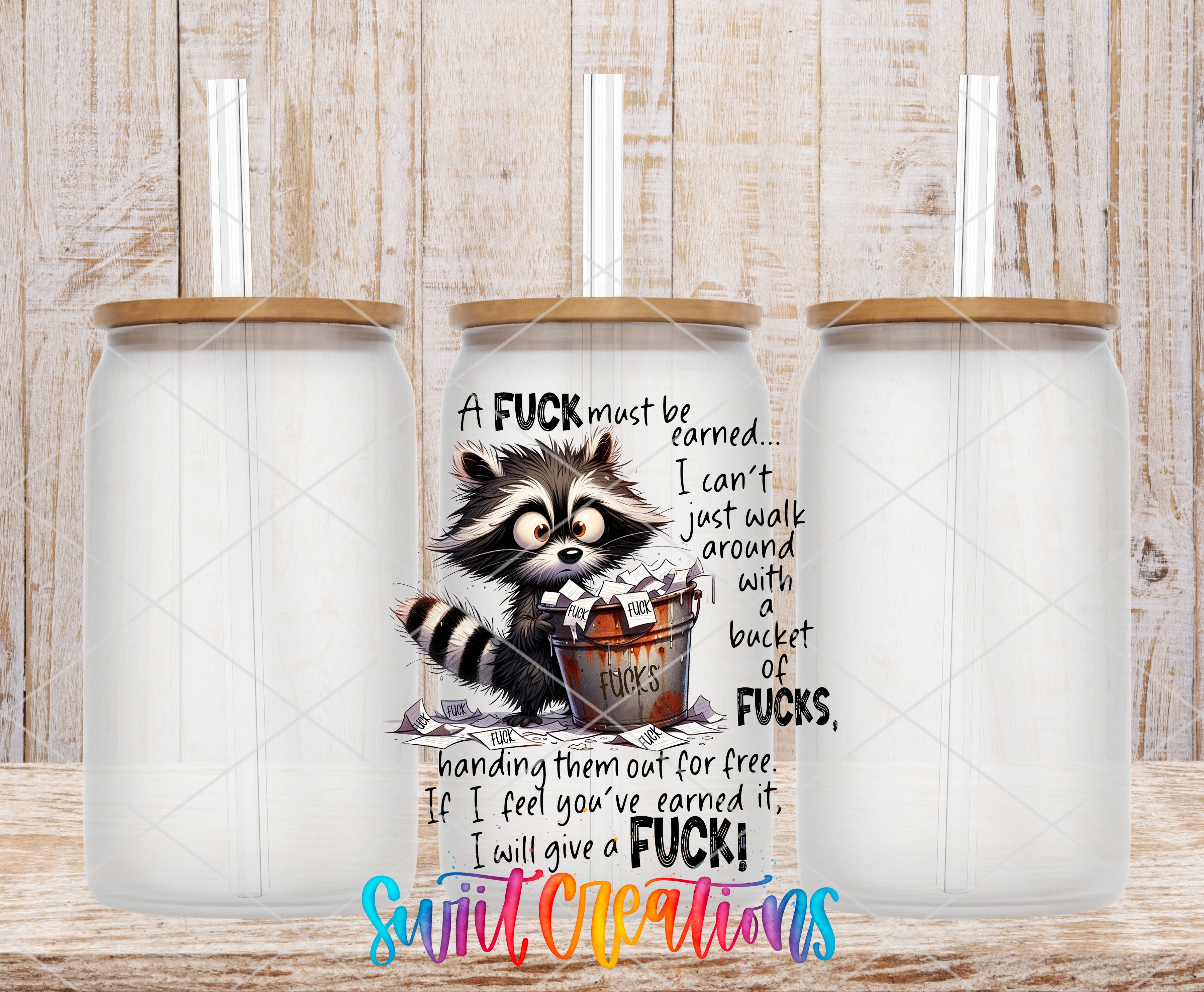 A cup with a raccoon design and text, along with three empty cups, against a wooden background.