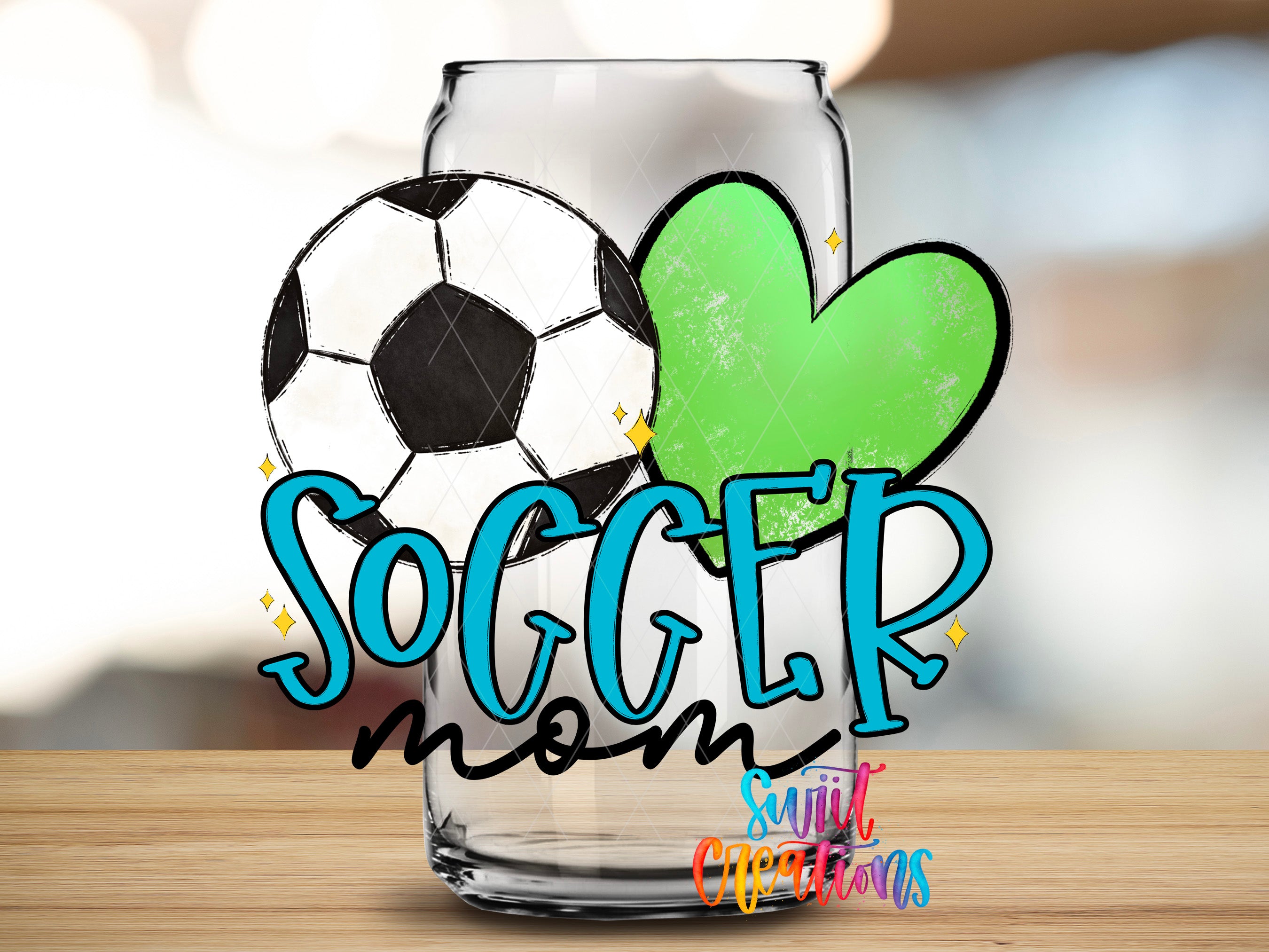 A glass can with a soccer ball and a heart-shaped green object, along with the text "SOCCER mom" and "Suitcase Creations" written on it.