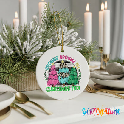A white Christmas tree ornament with a colorful design hangs on a table, surrounded by candles and greenery.