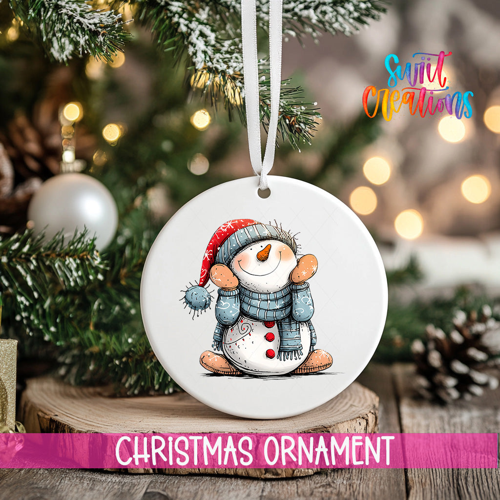 A white Christmas ornament featuring a snowman is hanging from a ribbon, with a blurred background of a decorated Christmas tree and other ornaments.