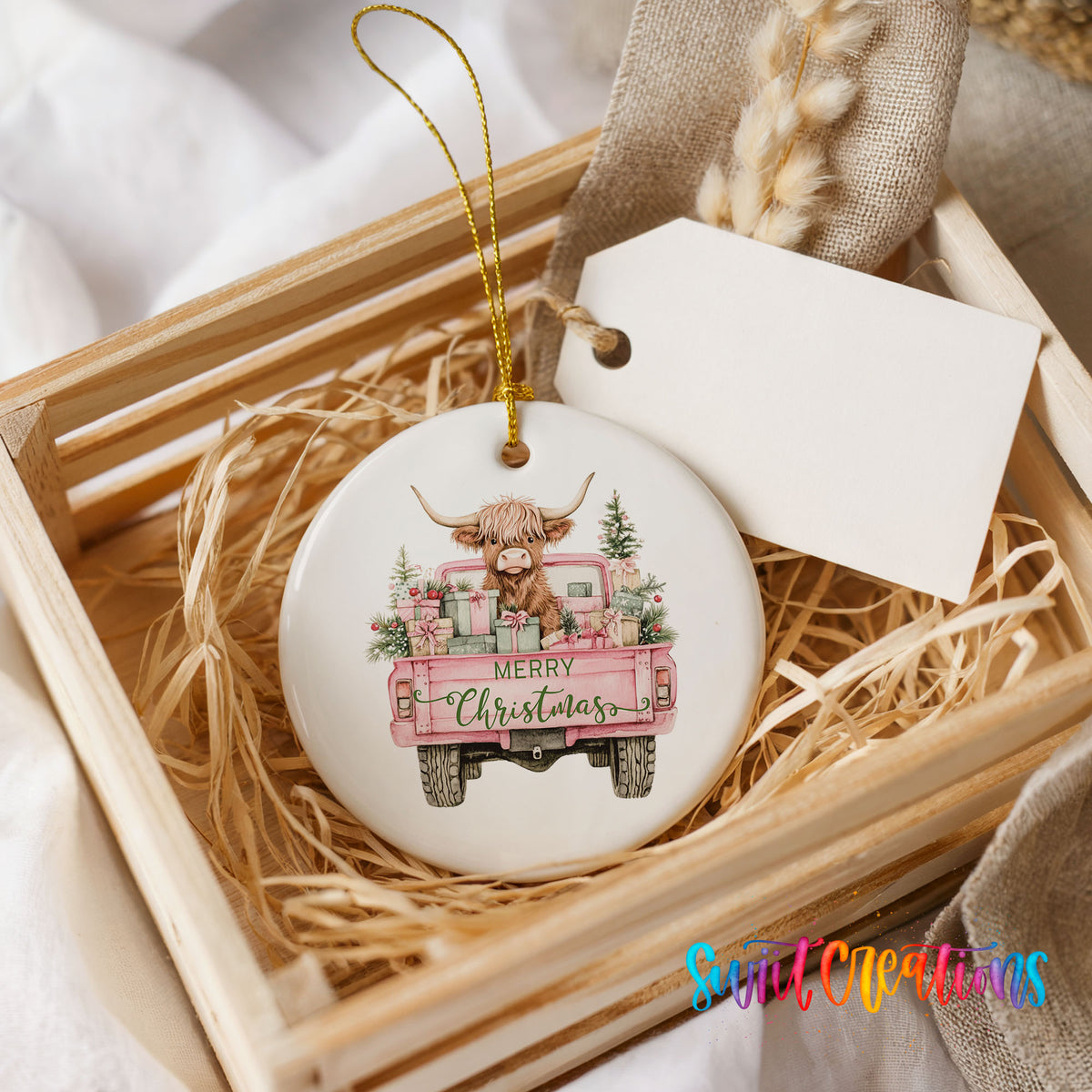 A ceramic ornament in a wooden crate, featuring a cartoon cow with horns and a Christmas tree in the back of a pink truck.