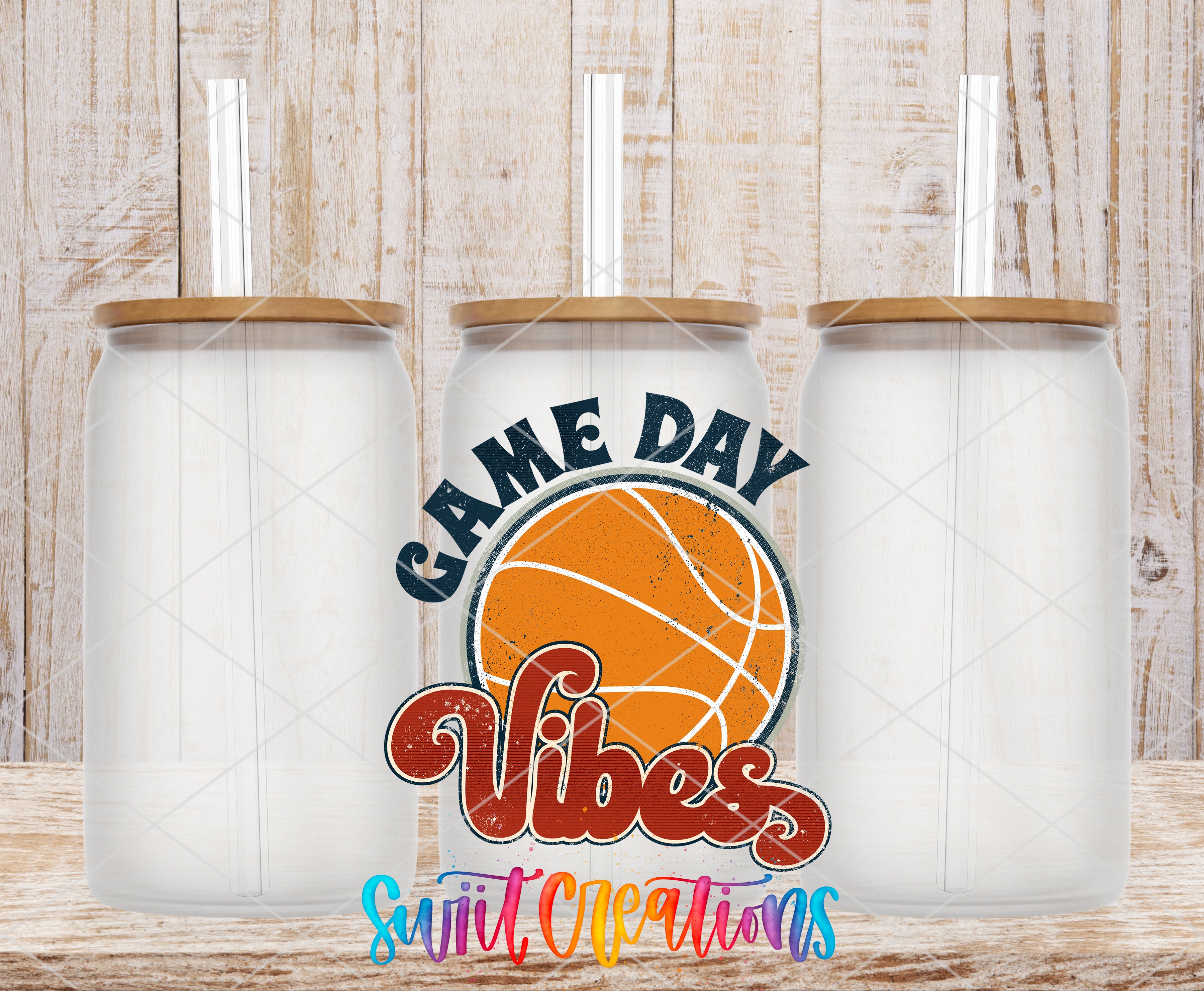 three clear glass tumblers with wooden lids, arranged in a row against a wooden background. The tumblers have straws sticking out of the tops. In the center of the image, there is a basketball graphic with the text "GAME DAY VIBES" written around it.