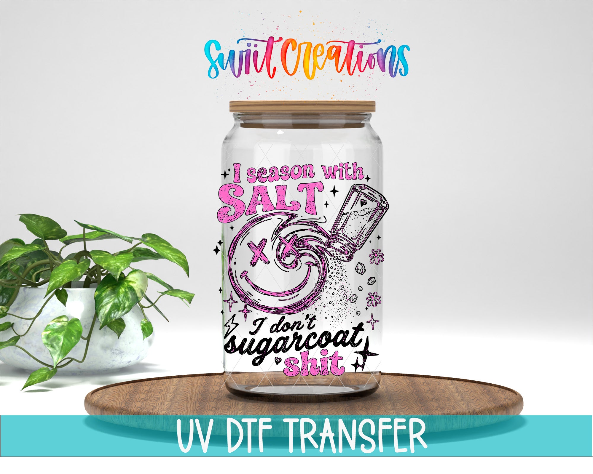 a glass jar with a colorful design and text, placed on a wooden surface next to a potted plant.