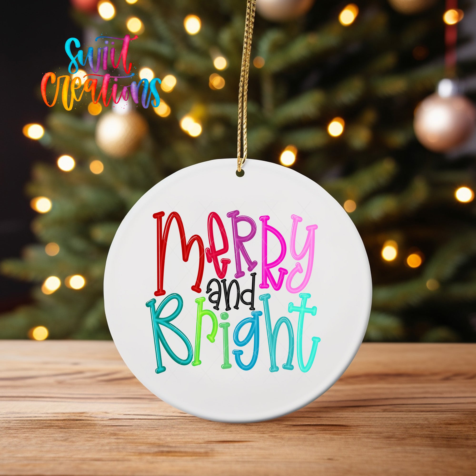 A white ceramic ornament with the text "Merry and Bright" written on it, hanging from a string. The ornament is placed on a wooden surface, with a blurred background of a Christmas tree and colorful lights.