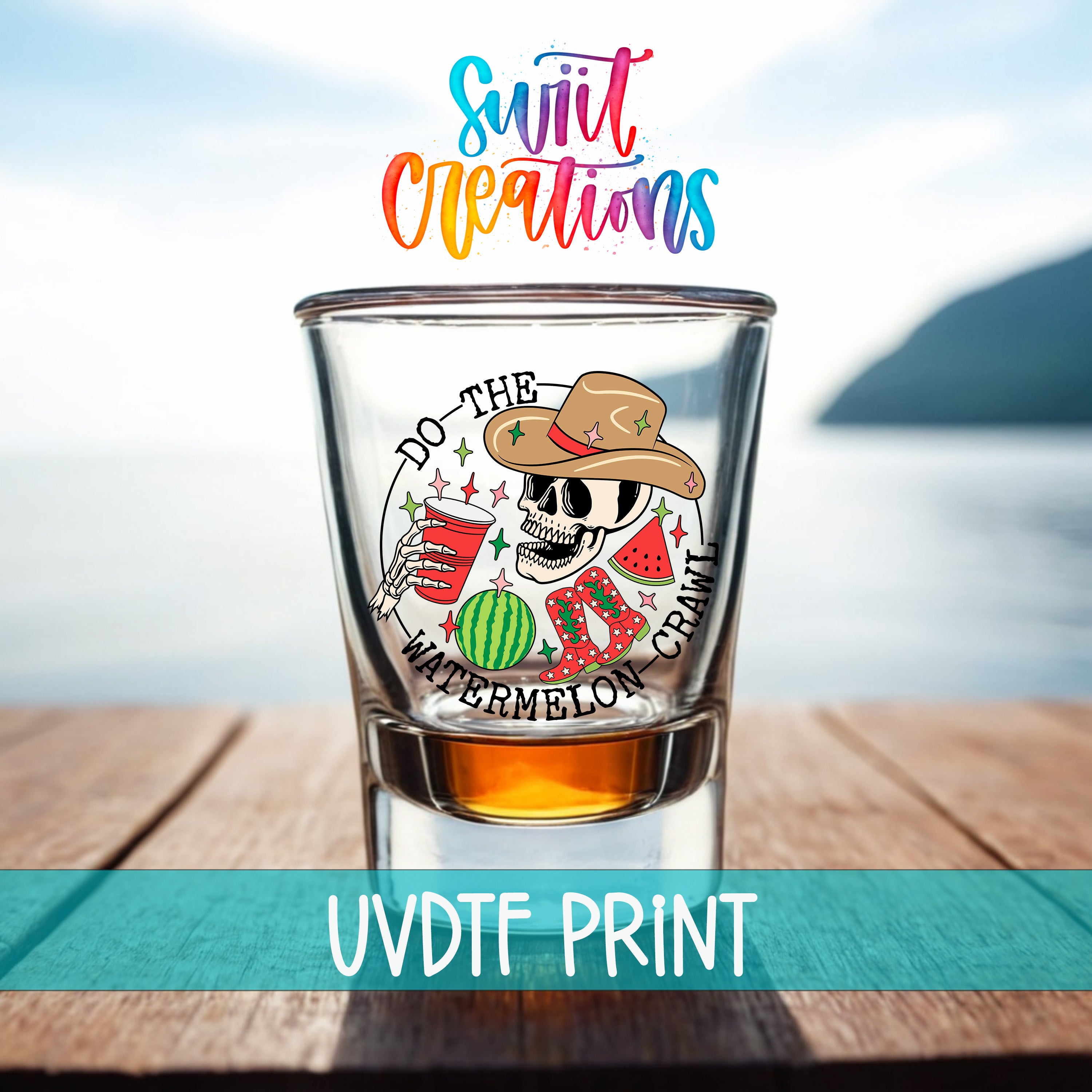 a shot glass with a colorful design and text, placed on a wooden surface with a body of water in the background.