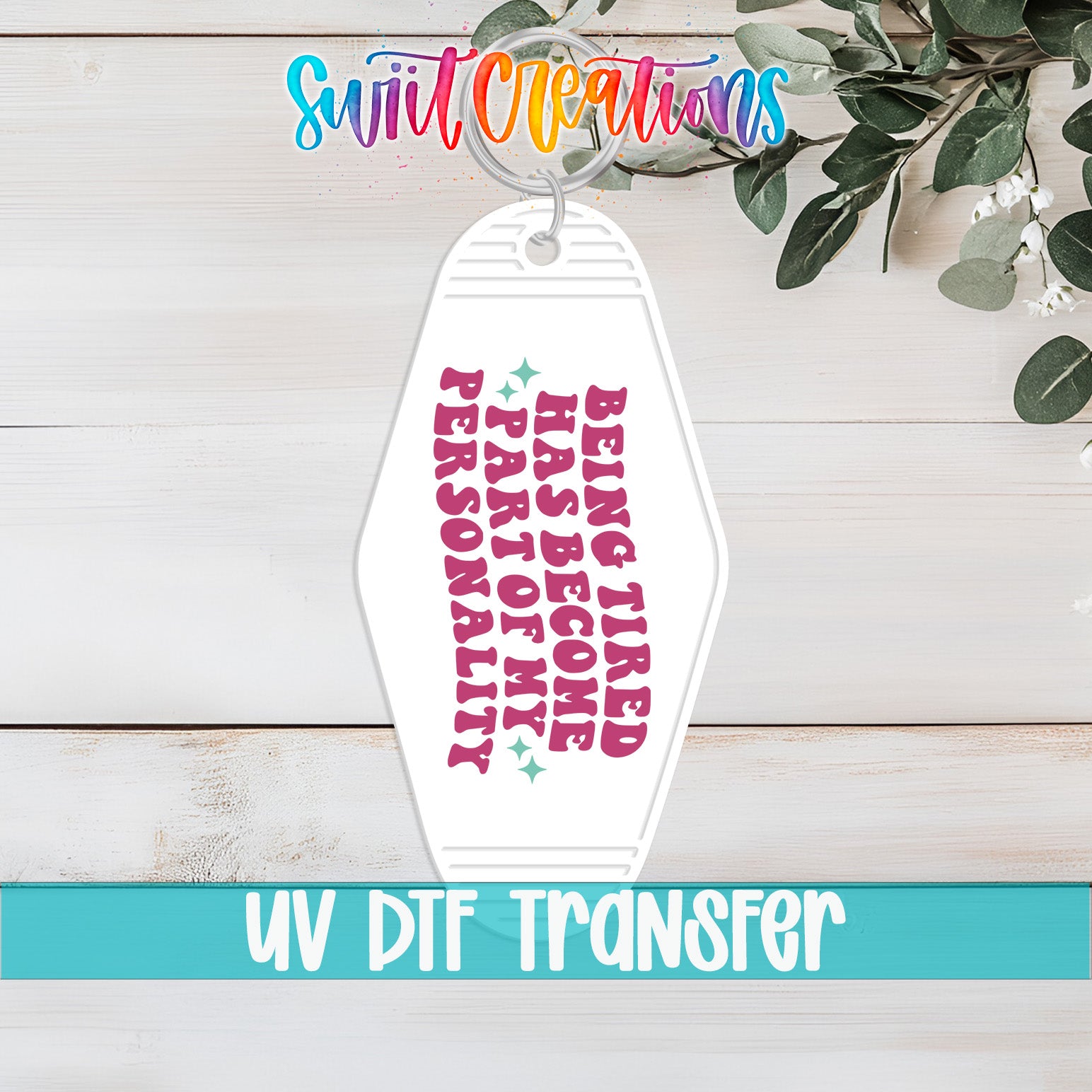 A keychain with a message printed on it, placed on a wooden surface with some greenery in the background.