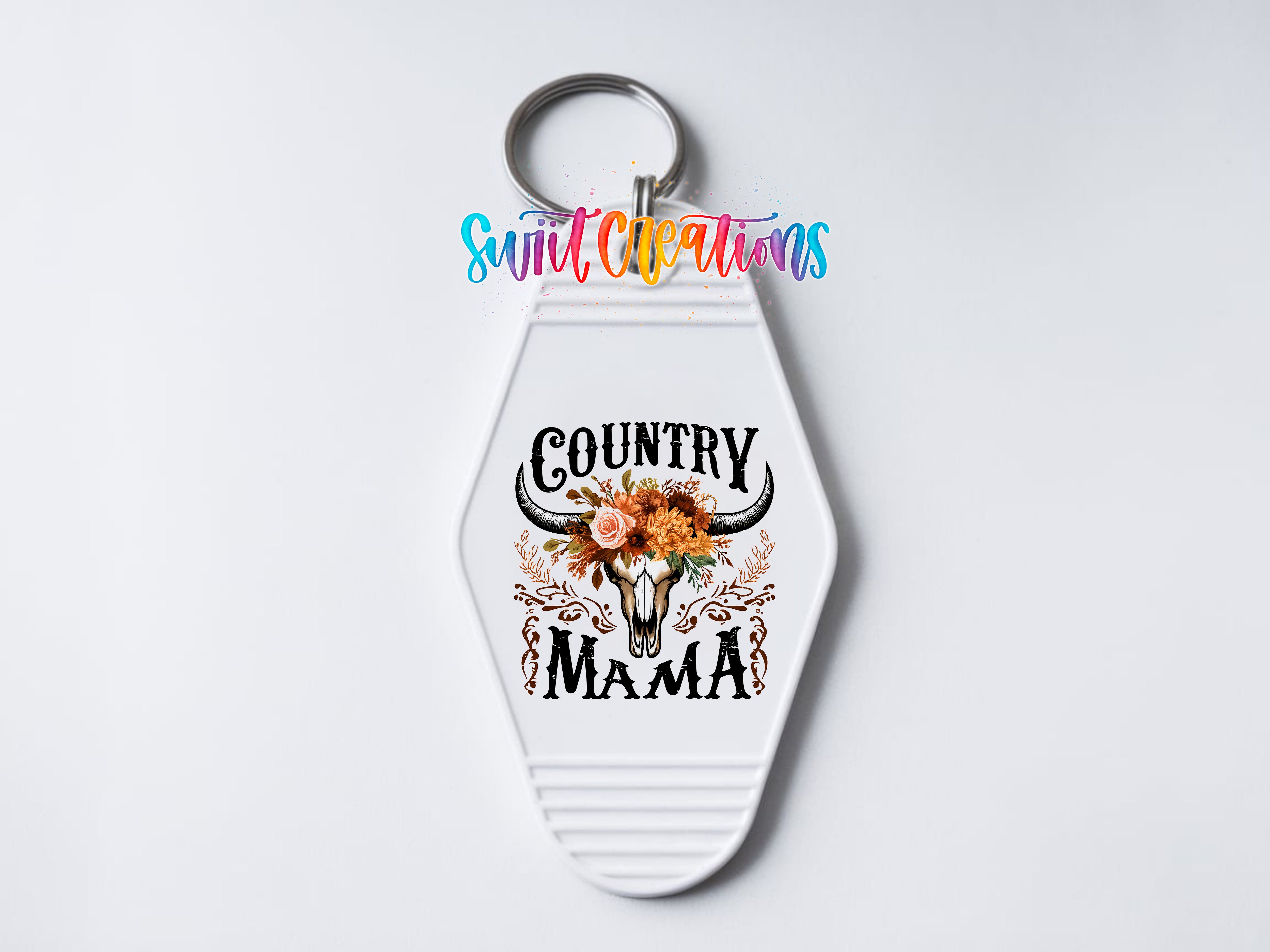 A keychain with a decorative design featuring a skull with horns and flowers, along with the text "COUNTRY MAMA" printed on it.