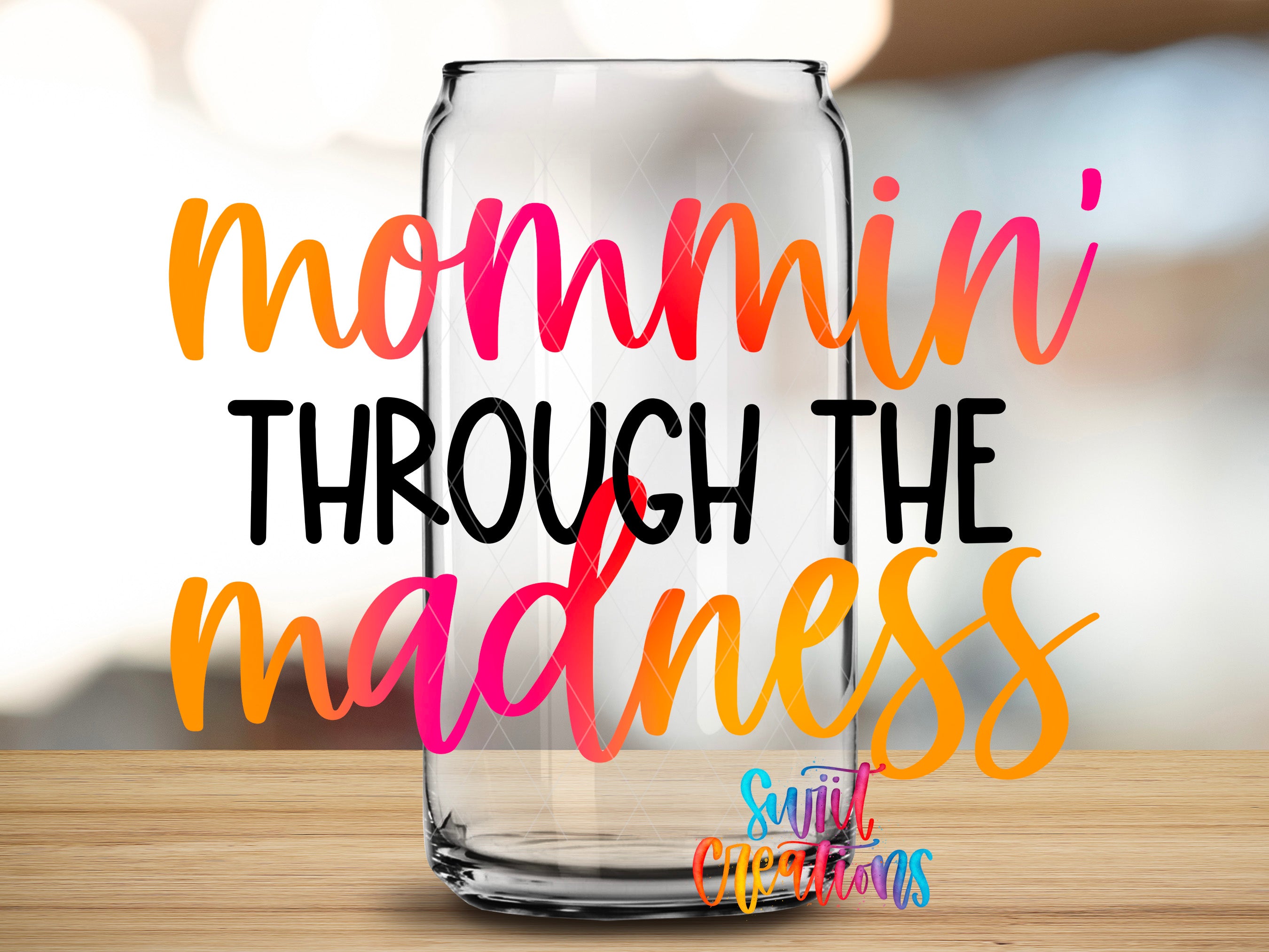 a clear glass can with the text "mommin' THROUGH THE MADNESS" written on it in a colorful, artistic style.