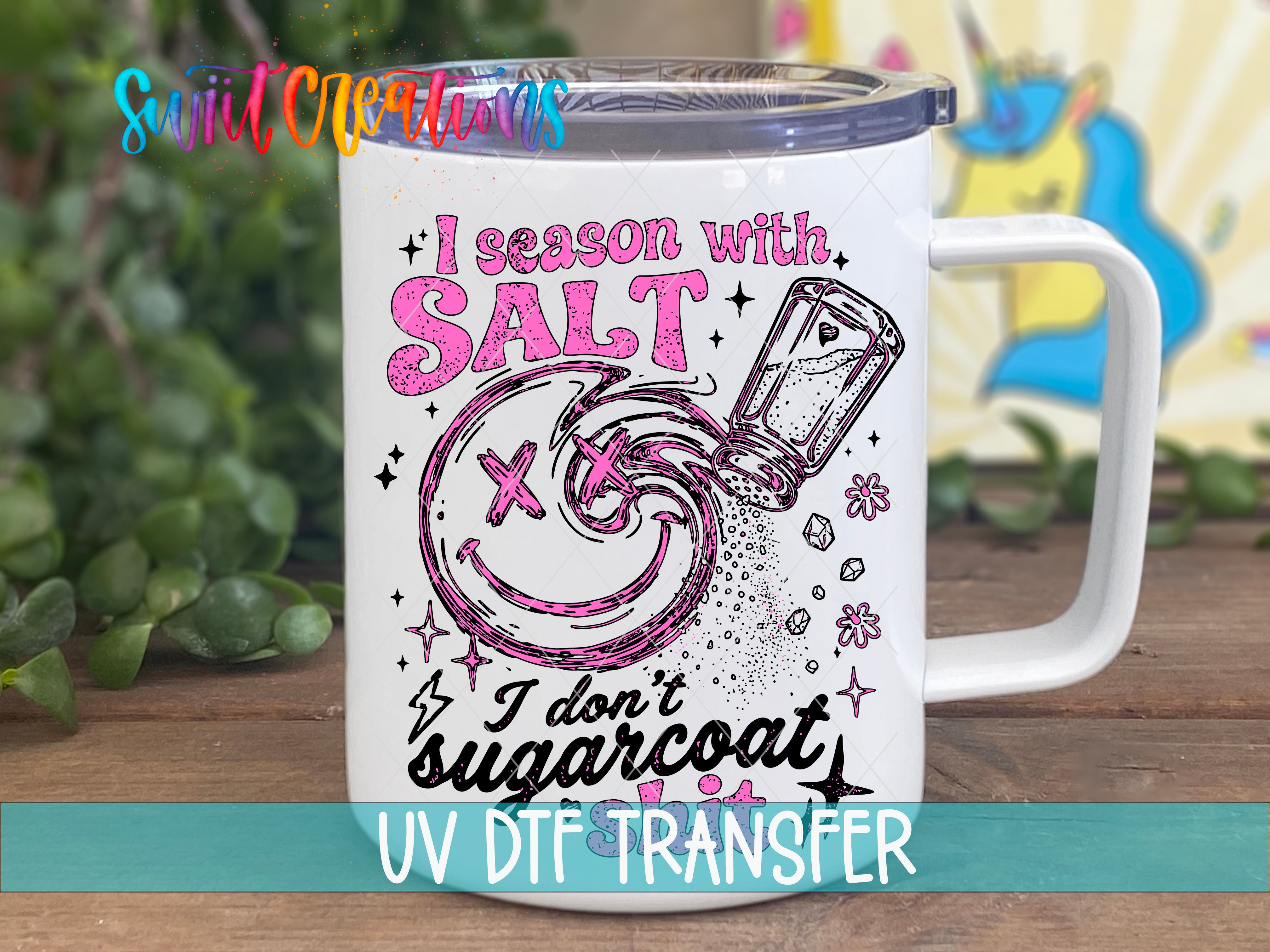 A white mug with a colorful design featuring a smiling face, a salt shaker, and text that reads "I season with salt" and "I don't sugarcoat".