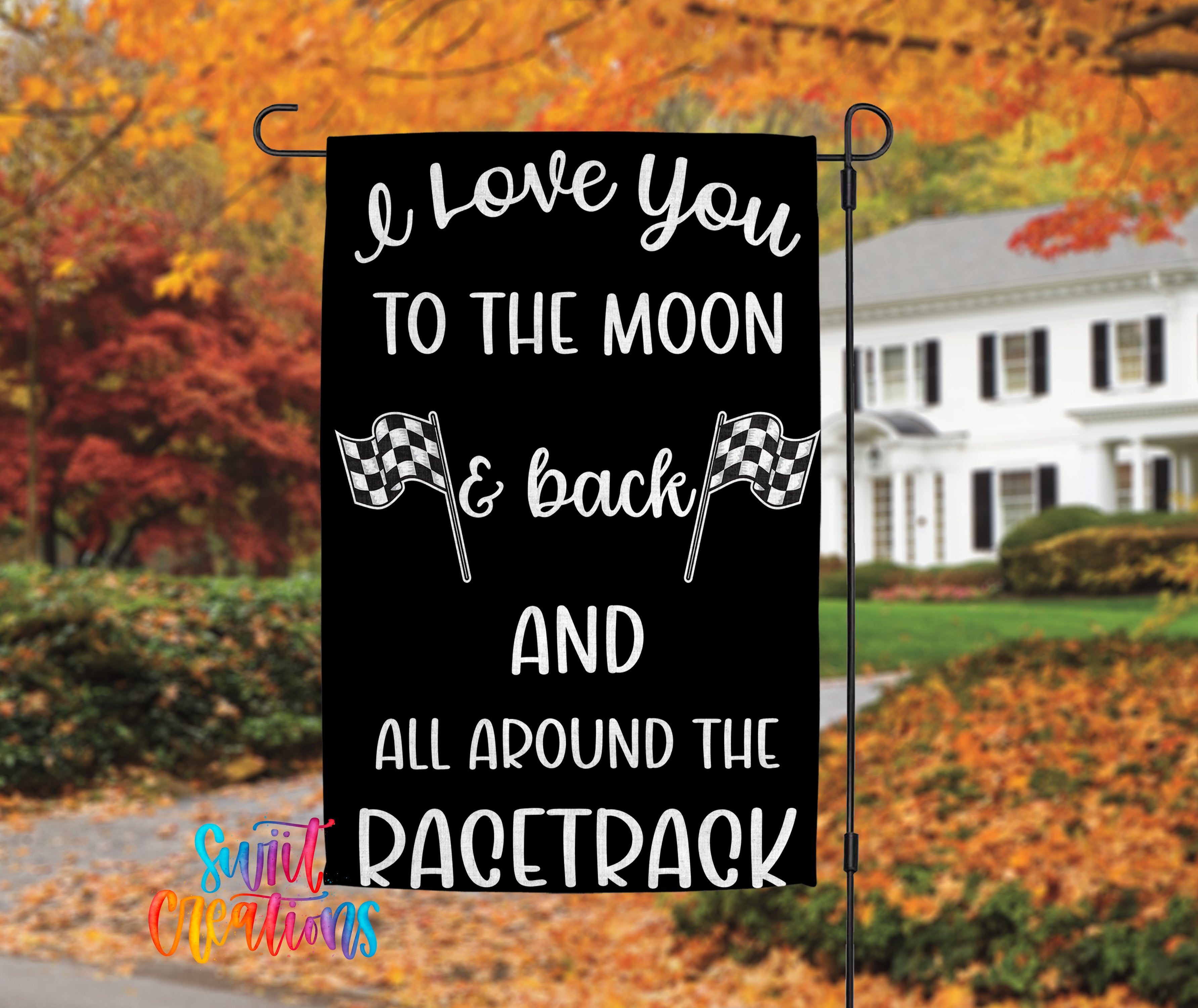 A black and white banner with text that reads "I love you to the moon & back AND all around the racetrack" is displayed in front of a house with autumn foliage in the background.