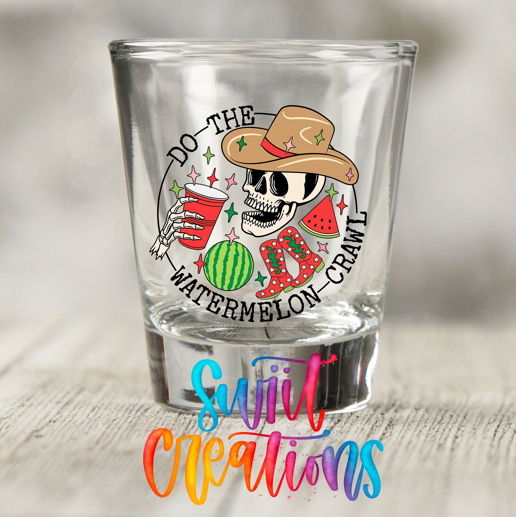 A shot glass with a skull wearing a cowboy hat and holding a watermelon and a red cup, surrounded by colorful text and graphics.