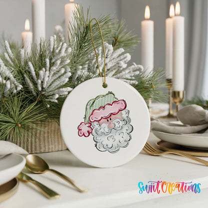 A white ceramic ornament with a Santa Claus face design is displayed on a table, surrounded by candles and greenery.
