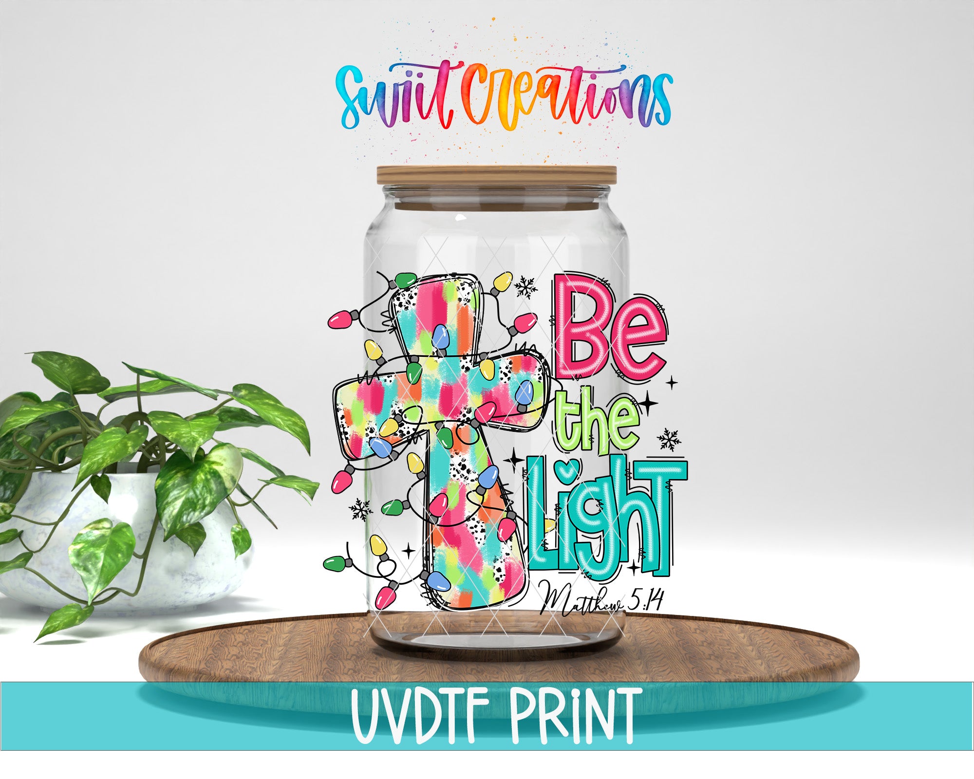 A colorful illustration of a cross surrounded by Christmas lights, with the text "Be the light" and "Swift Creations" written above it. The image is displayed on a wooden tray, and there is a potted plant in the background.