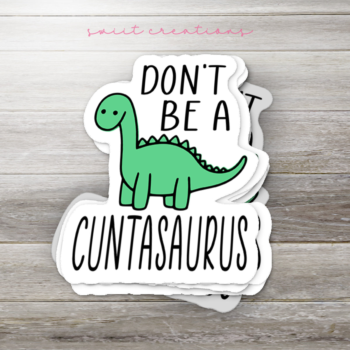 Stack of Don't Be a C*ntasaurus glossy stickers on a gray wood table