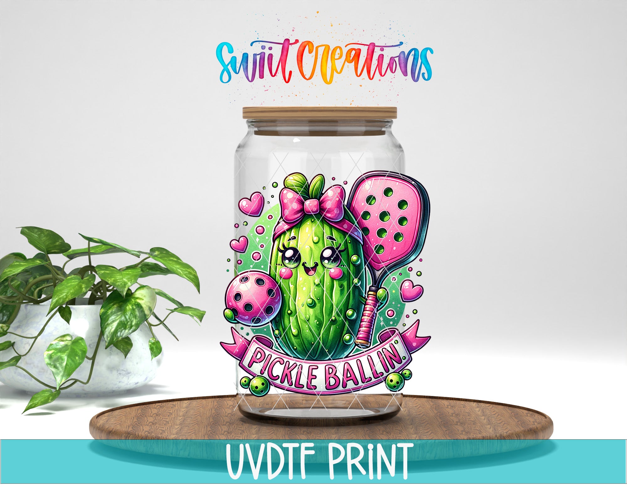 A glass jar with a colorful illustration of a pickle and a bow, along with the text "Pickle Ballin" and the logo "Swift Creations". The jar is placed on a wooden surface, and there is a potted plant in the background.