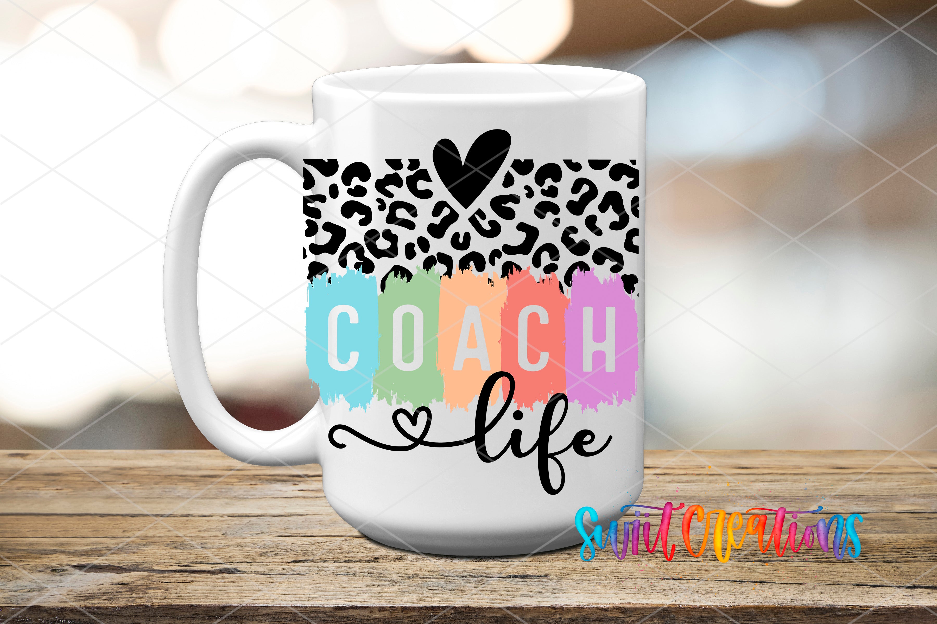 A white coffee mug with a leopard print design and the word "COACH" written in colorful paint strokes.