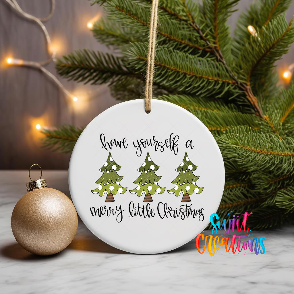 A white ceramic ornament with a Christmas tree design and the text "Have yourself a merry little Christmas" is displayed on a marble surface, with a gold ornament and a pine tree in the background.