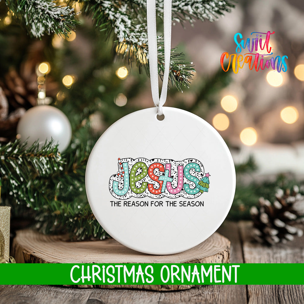 A white Christmas ornament with the word "JESUS" written on it, hanging from a tree branch.