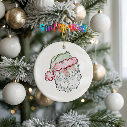 A white ceramic ornament with a Santa Claus face is hanging on a Christmas tree, surrounded by white and gold ornaments.