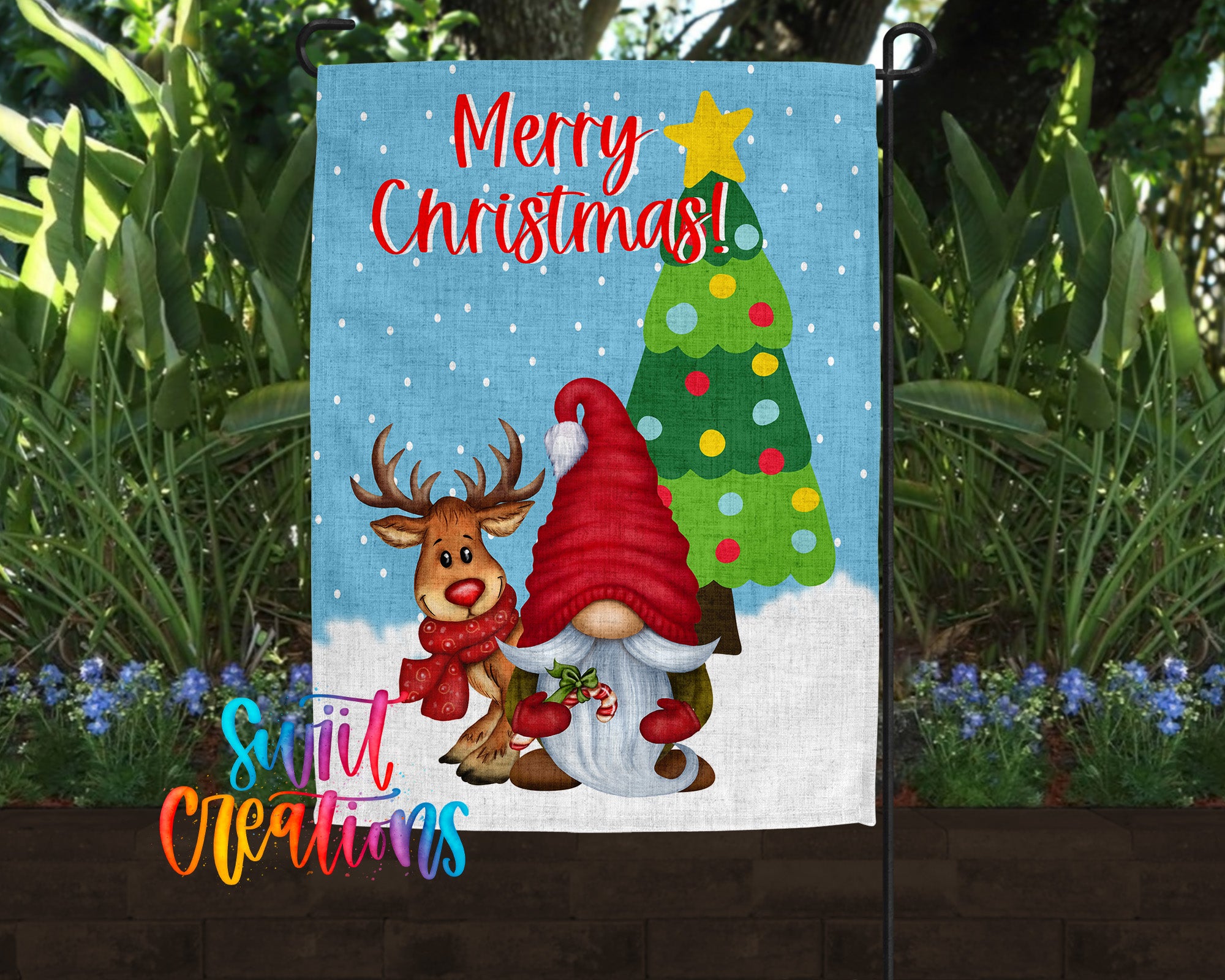 A Christmas-themed garden flag featuring a gnome and a reindeer, with a snow-covered landscape and a Christmas tree in the background.