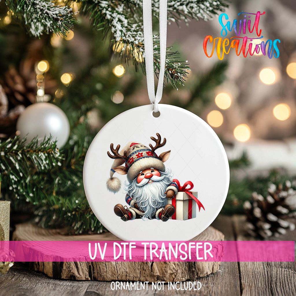 A white ornament with a Santa Claus image and a gift box is hanging on a Christmas tree.