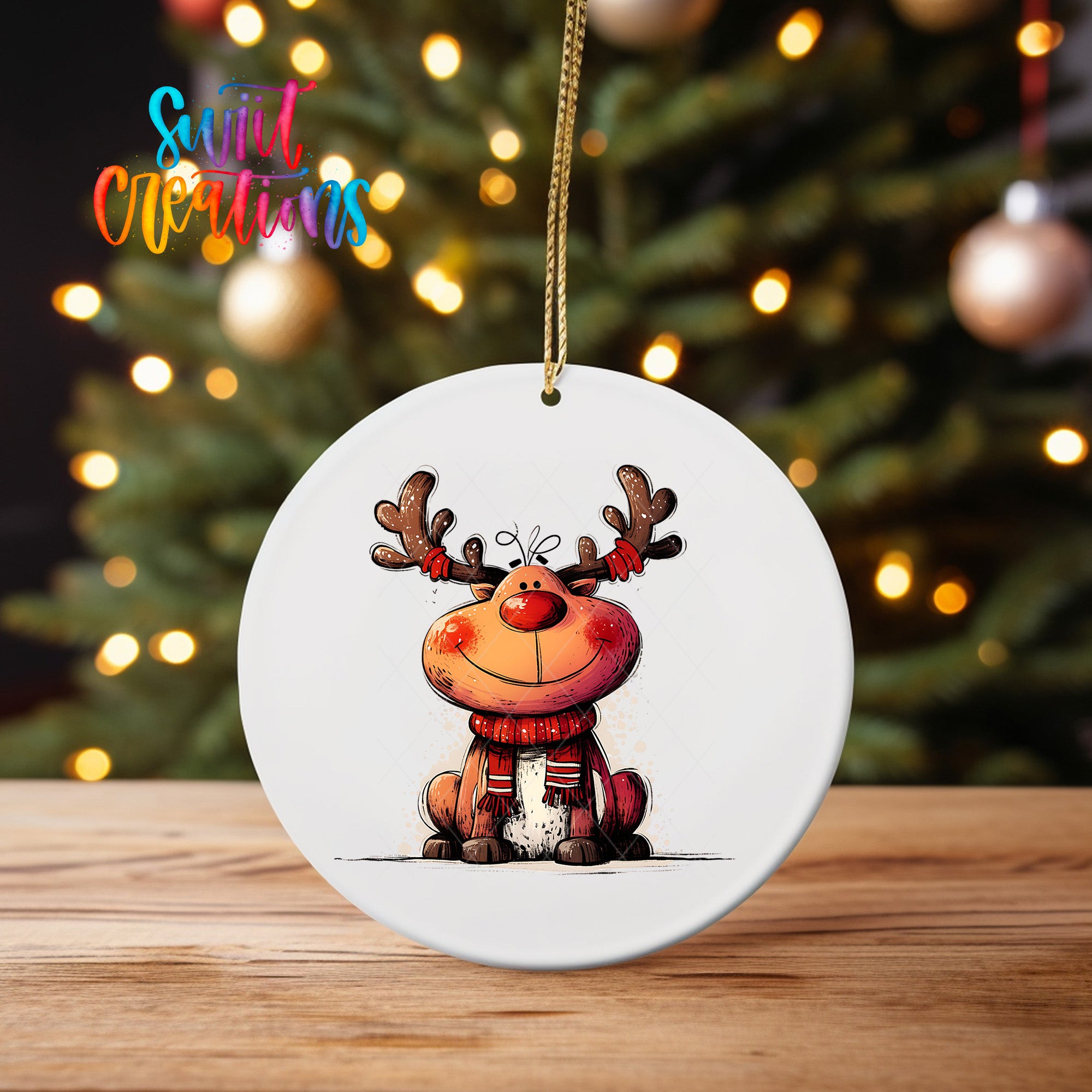 A white ceramic ornament featuring a cartoon reindeer with antlers and a red scarf, sitting on a wooden surface in front of a blurred Christmas tree with twinkling lights.