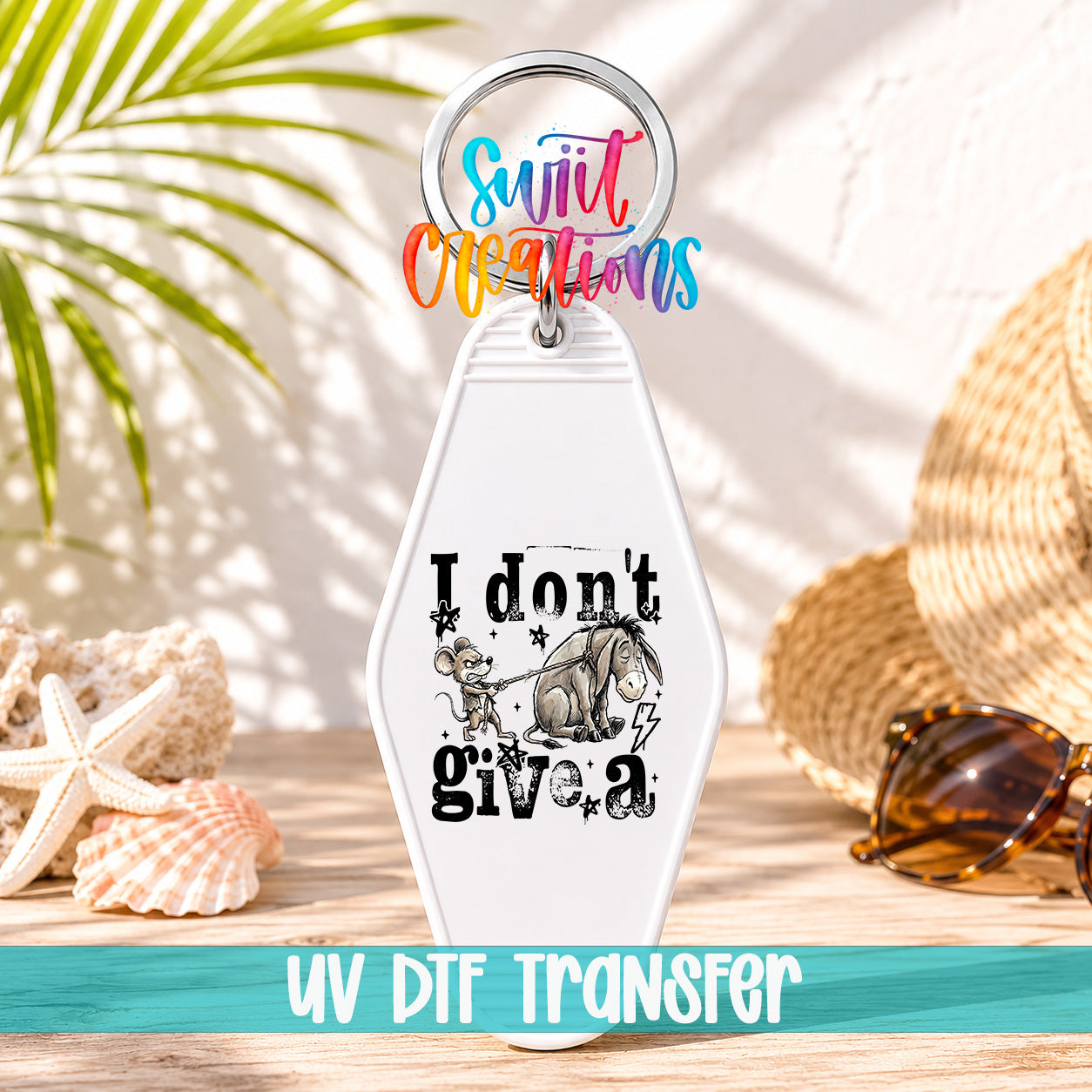 A keychain with a cartoon image of a mouse and the text "I don't give a" printed on it, along with a colorful ring and a straw hat. The keychain is placed on a wooden surface, with sunglasses and a starfish nearby.