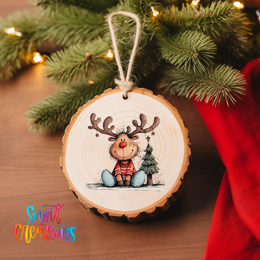 A wooden ornament featuring a cartoon reindeer with antlers, sitting next to a Christmas tree, is hanging on a tree branch.