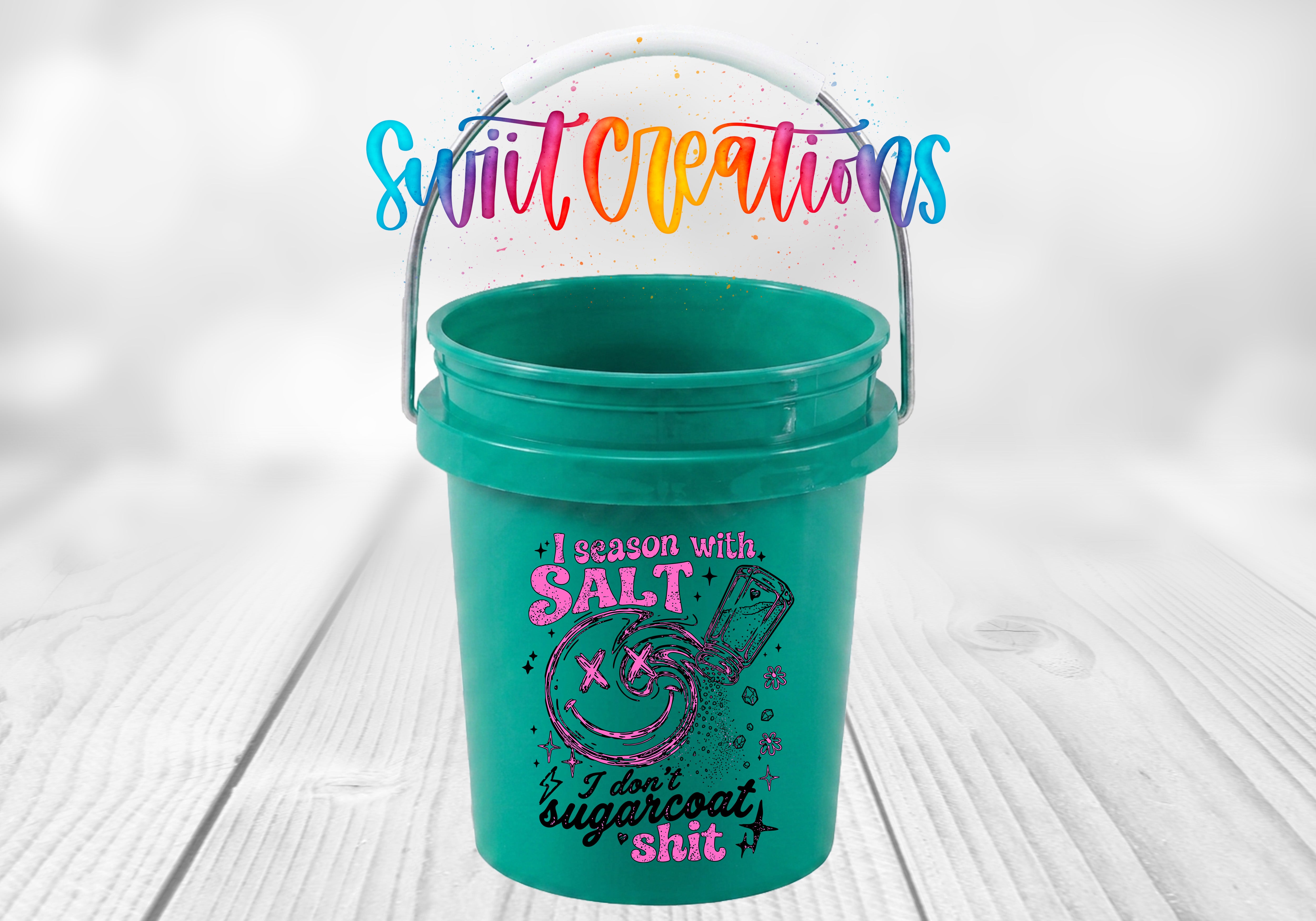 A green bucket with a colorful design and text printed on it, placed on a wooden surface.