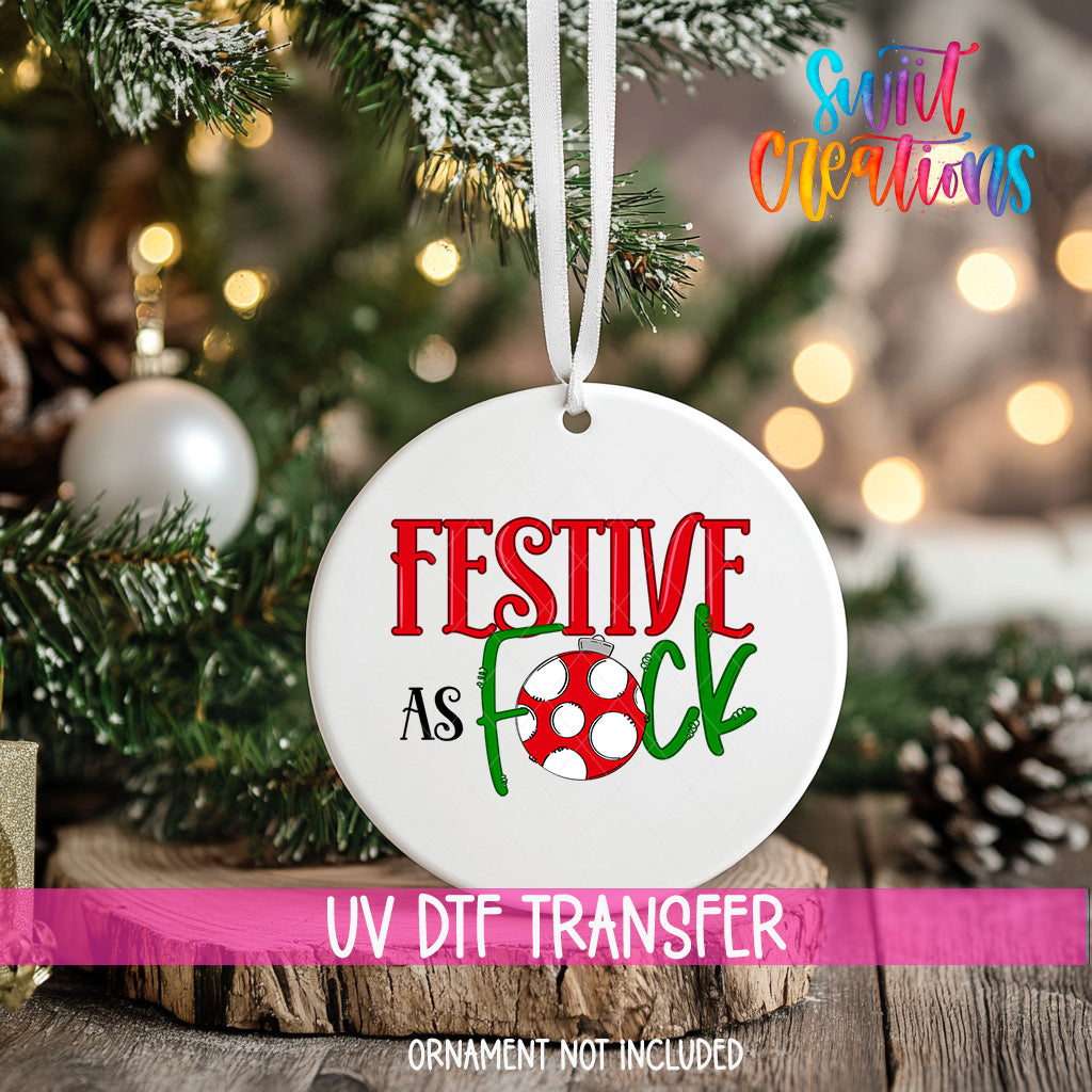 A white ornament with the text "FESTIVE AS FOCK" and a red and green polka dot design hangs on a Christmas tree.
