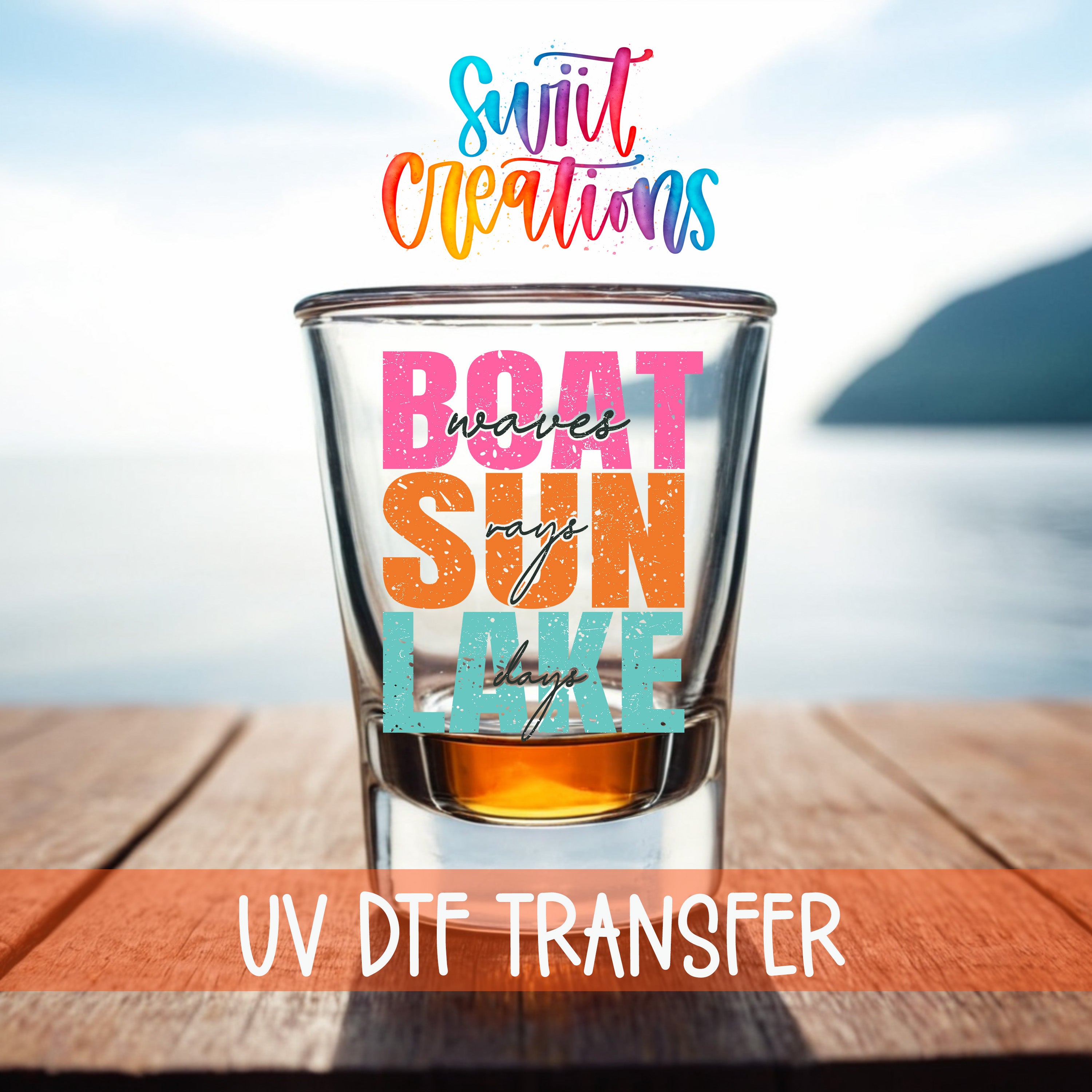 a glass of amber liquid with the text "BOAT SUN LAKE" and "UV DDF TRANSFER" written on it, placed on a wooden surface with a blurred background of a body of water and a mountain.