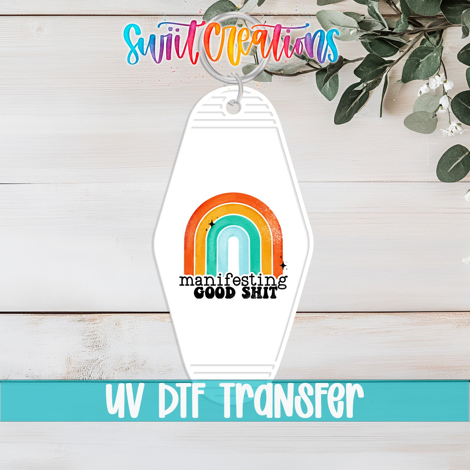 A keychain with a rainbow graphic and the text "manifesting good shit" printed on it, along with a UV DFT transfer label.
