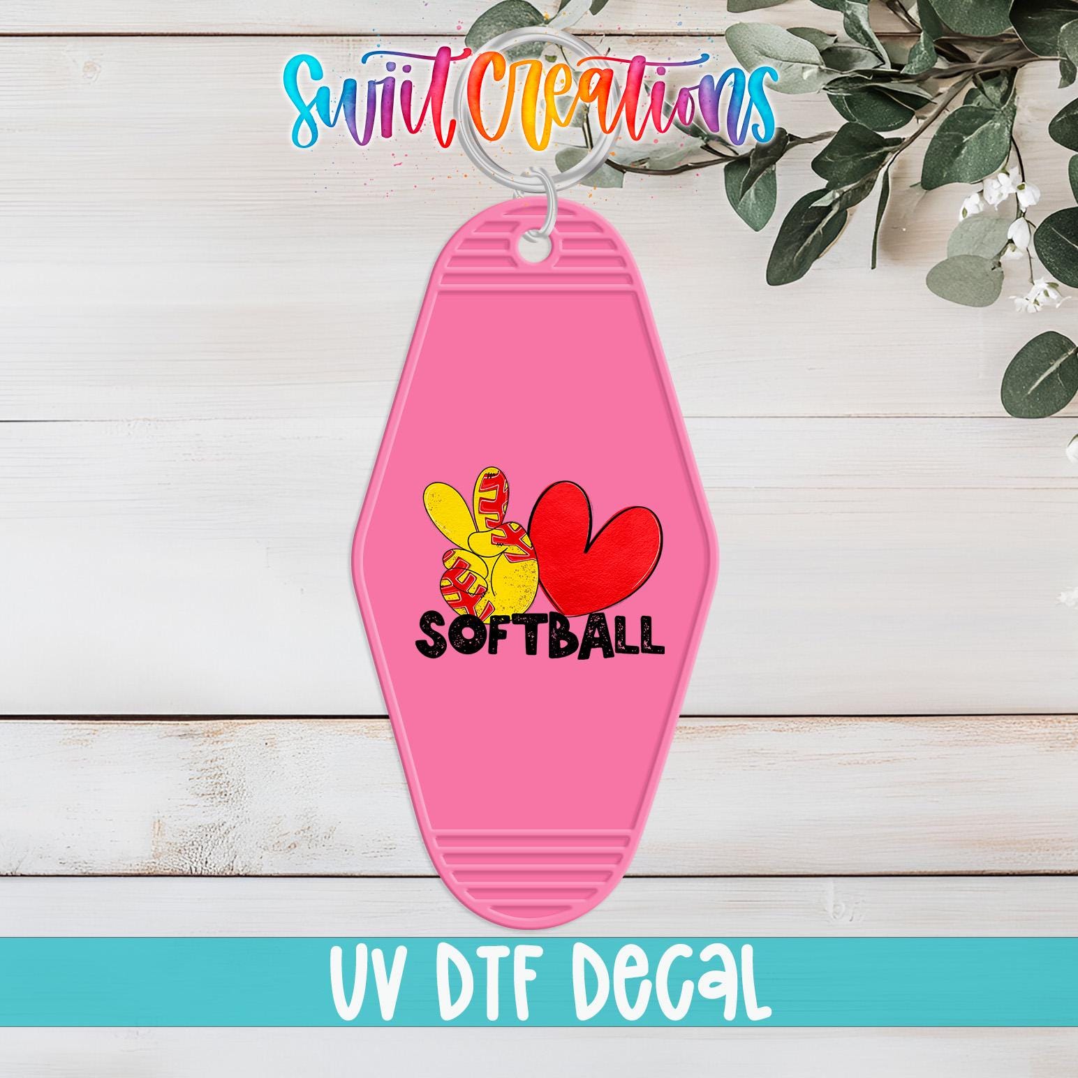 A pink keychain with a softball design and the text "SOFTBALL" printed on it, placed on a wooden surface with a plant in the background.