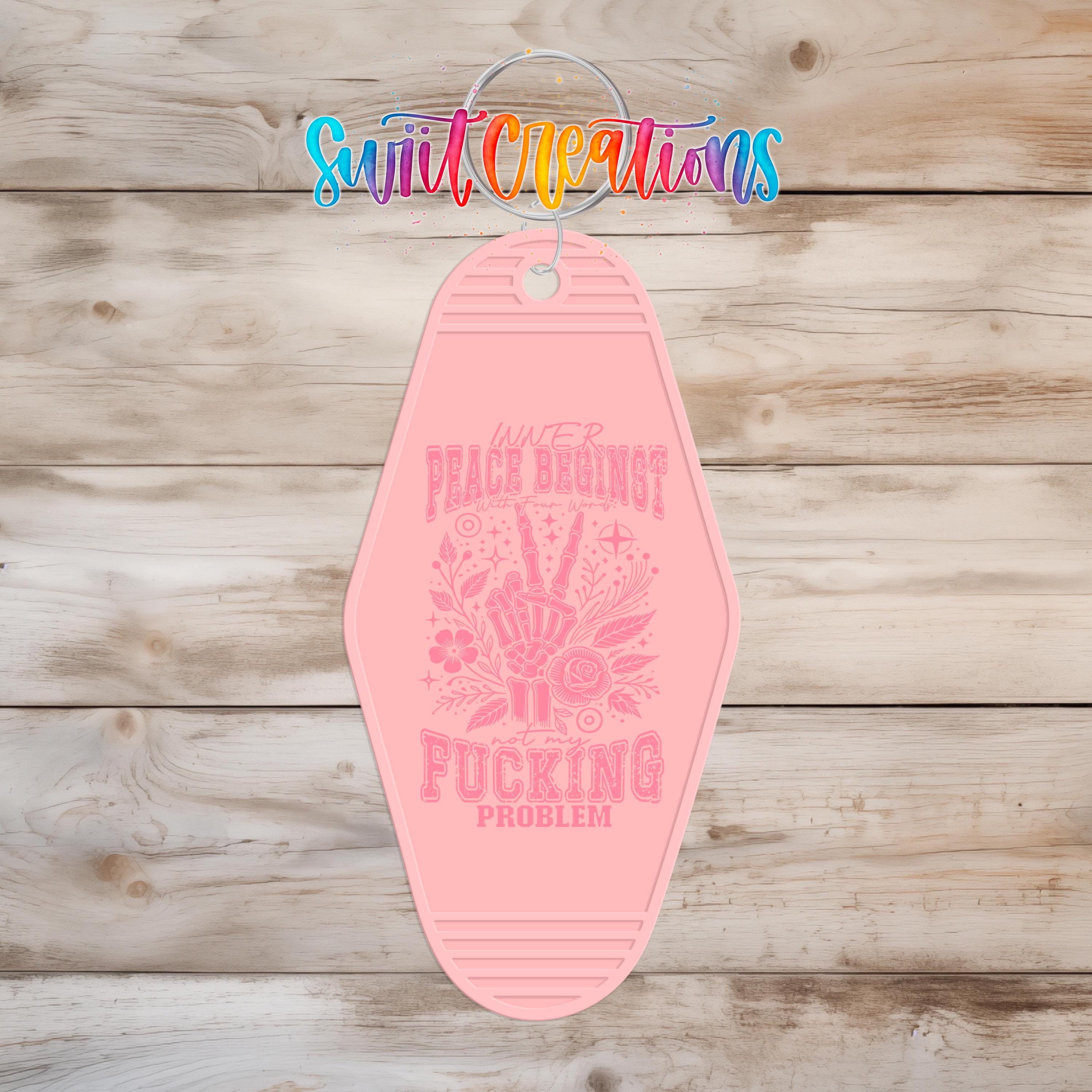 A pink keychain with a message printed on it, hanging on a wooden surface.