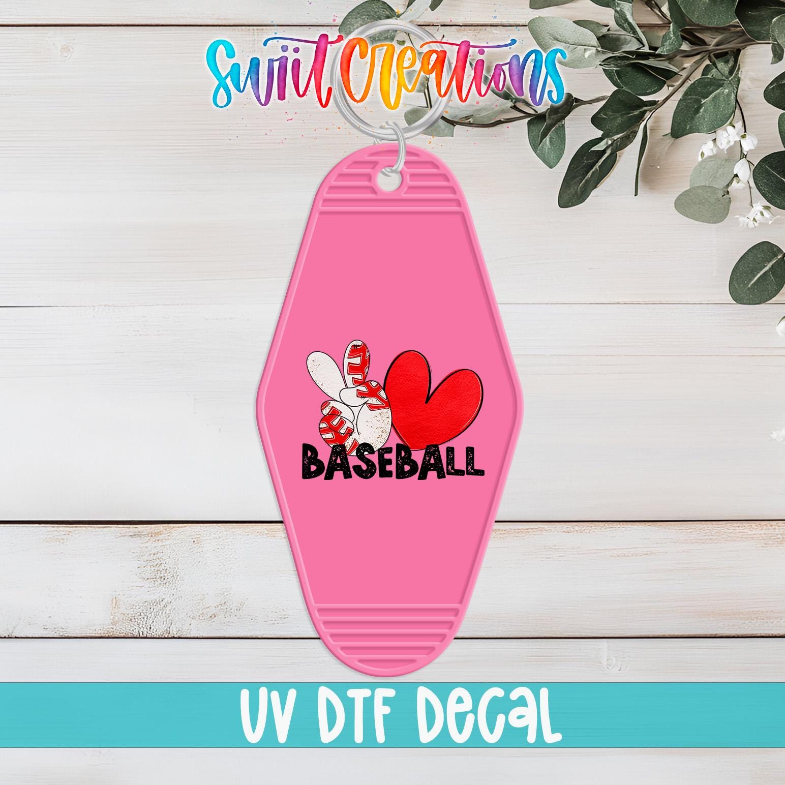 A pink keychain with a baseball design and the word "BASEBALL" printed on it, placed on a wooden surface with a plant in the background.